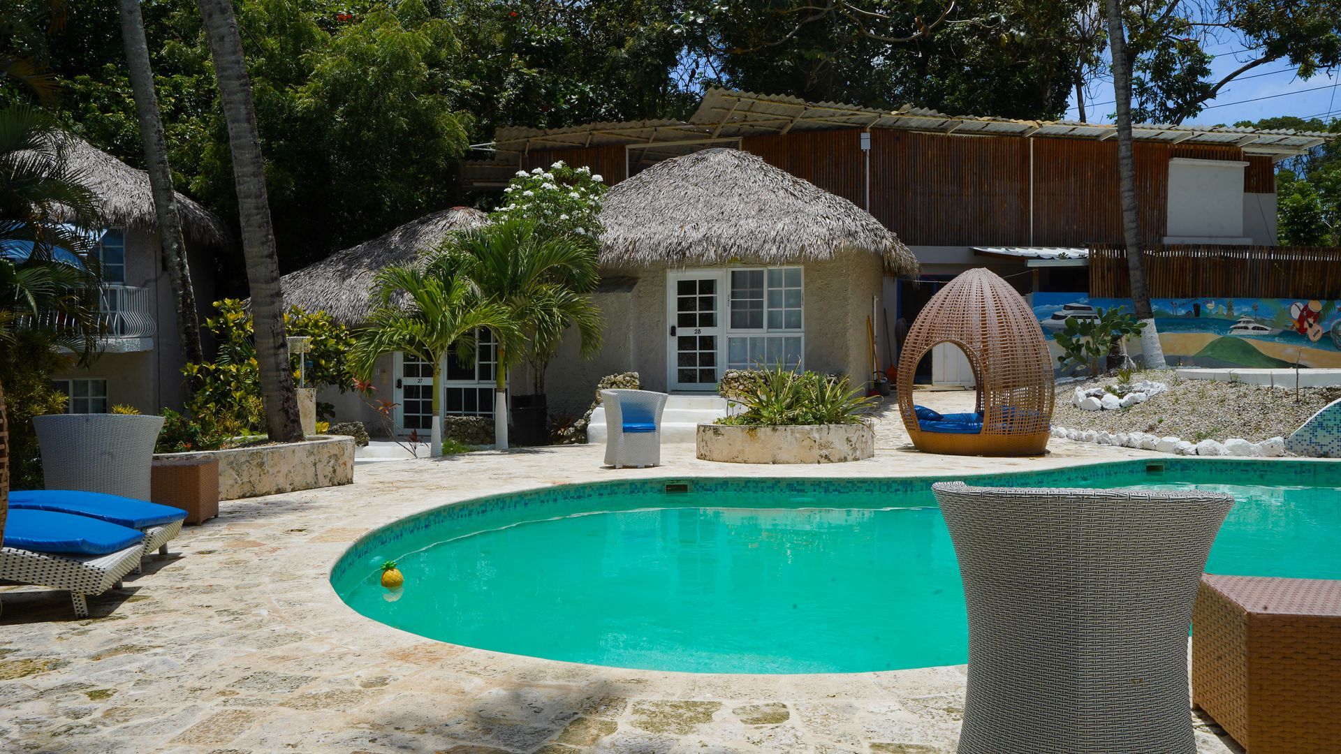 Resort pool with turquoise water, thatched hut, lounge chairs, and shaded cabana near palm trees