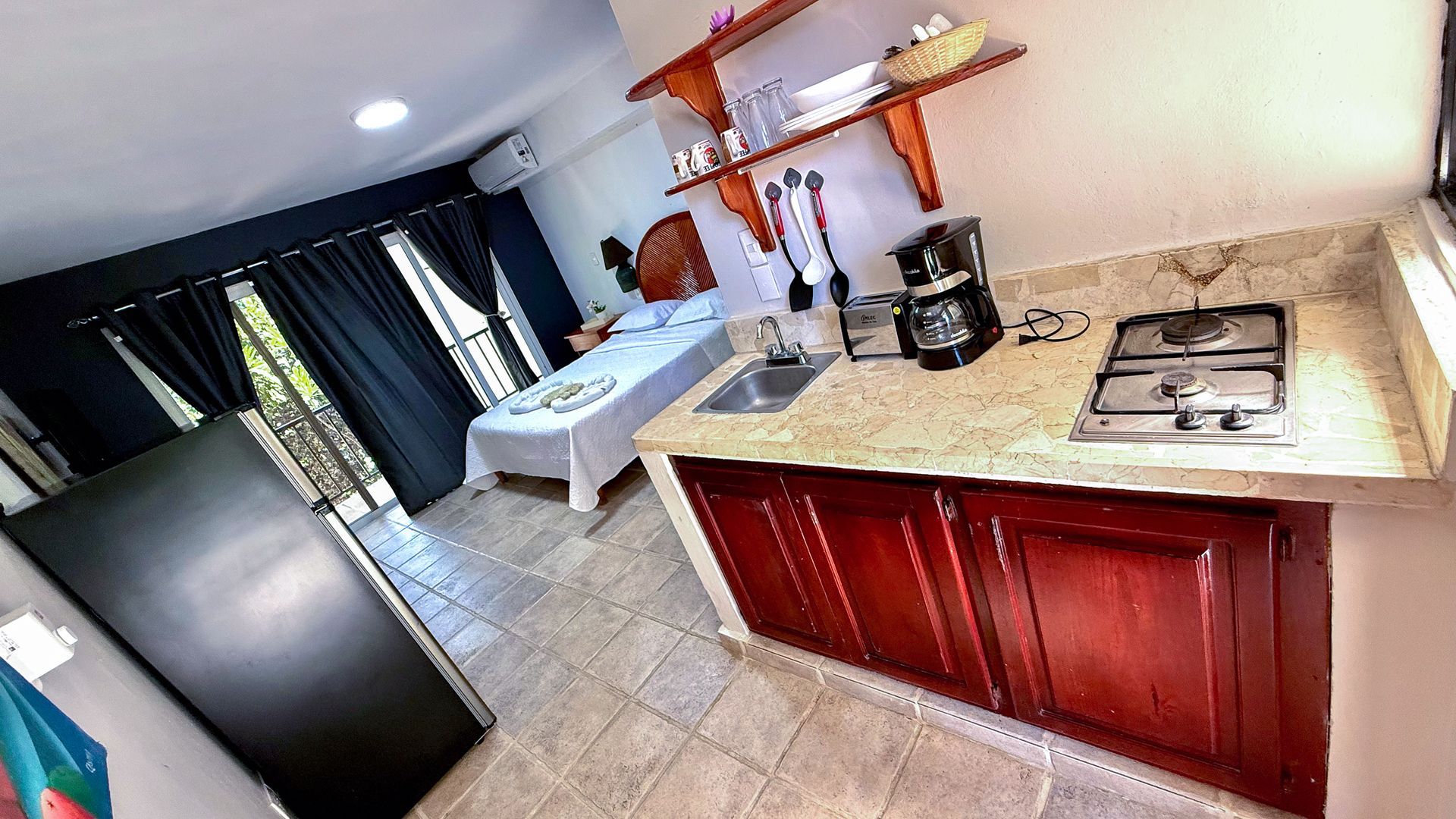 Modern kitchen with red cabinets, beige counters, stove, coffee maker, and dark curtains near the dining area