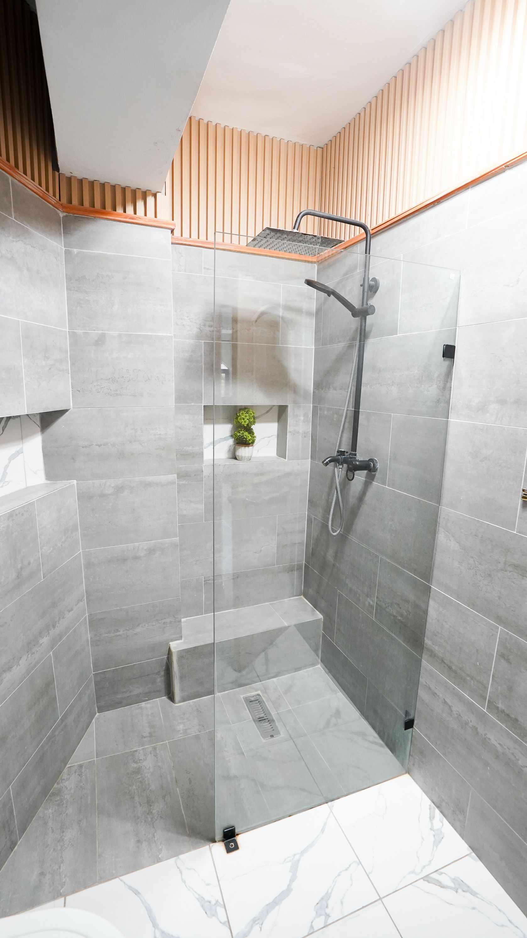 Modern shower stall with gray tile walls, glass door, white floor, and wall-mounted showerhead