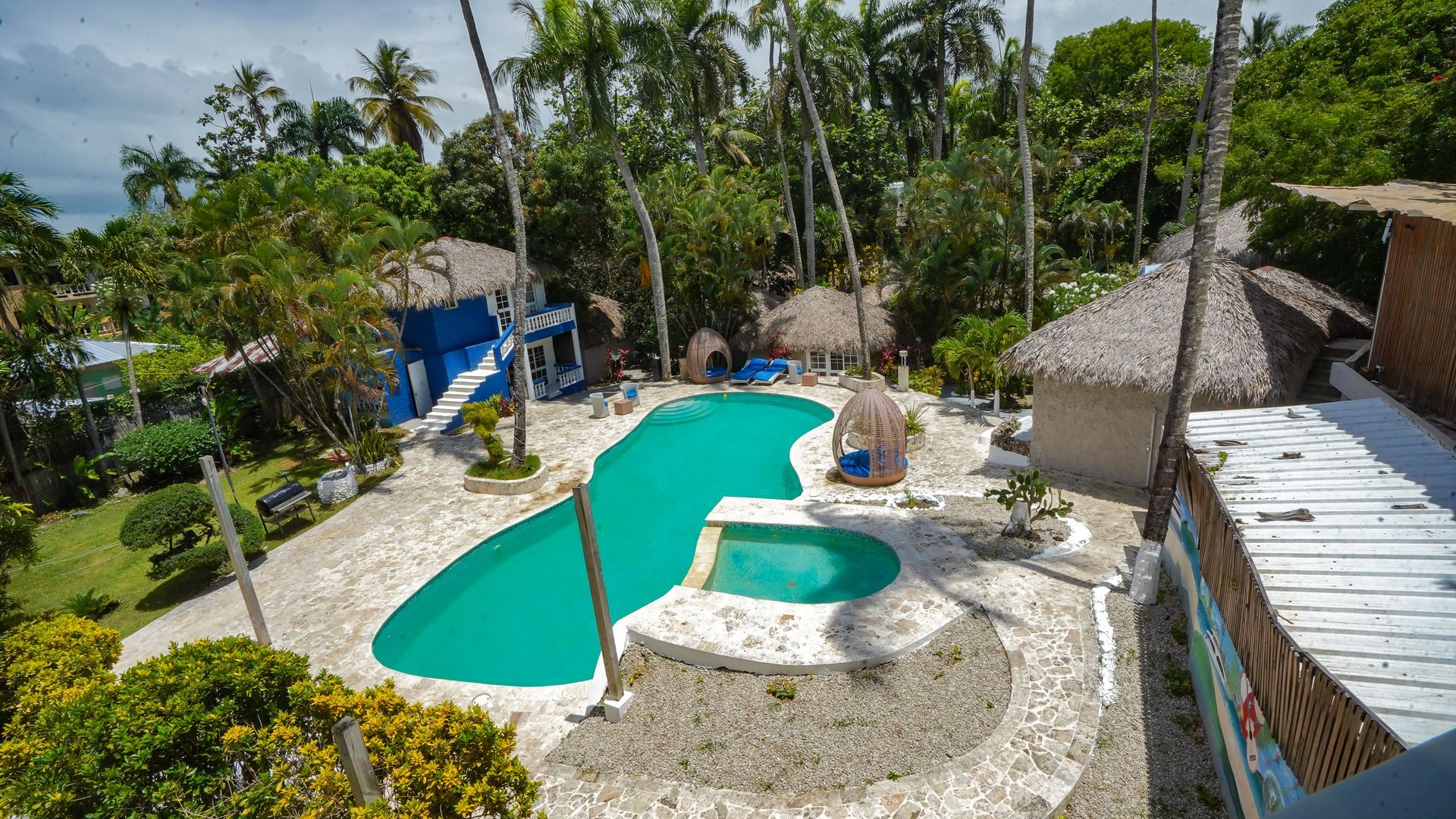 Tropical resort pool with a curving turquoise lagoon, palm trees, and thatched huts under sunny skies
