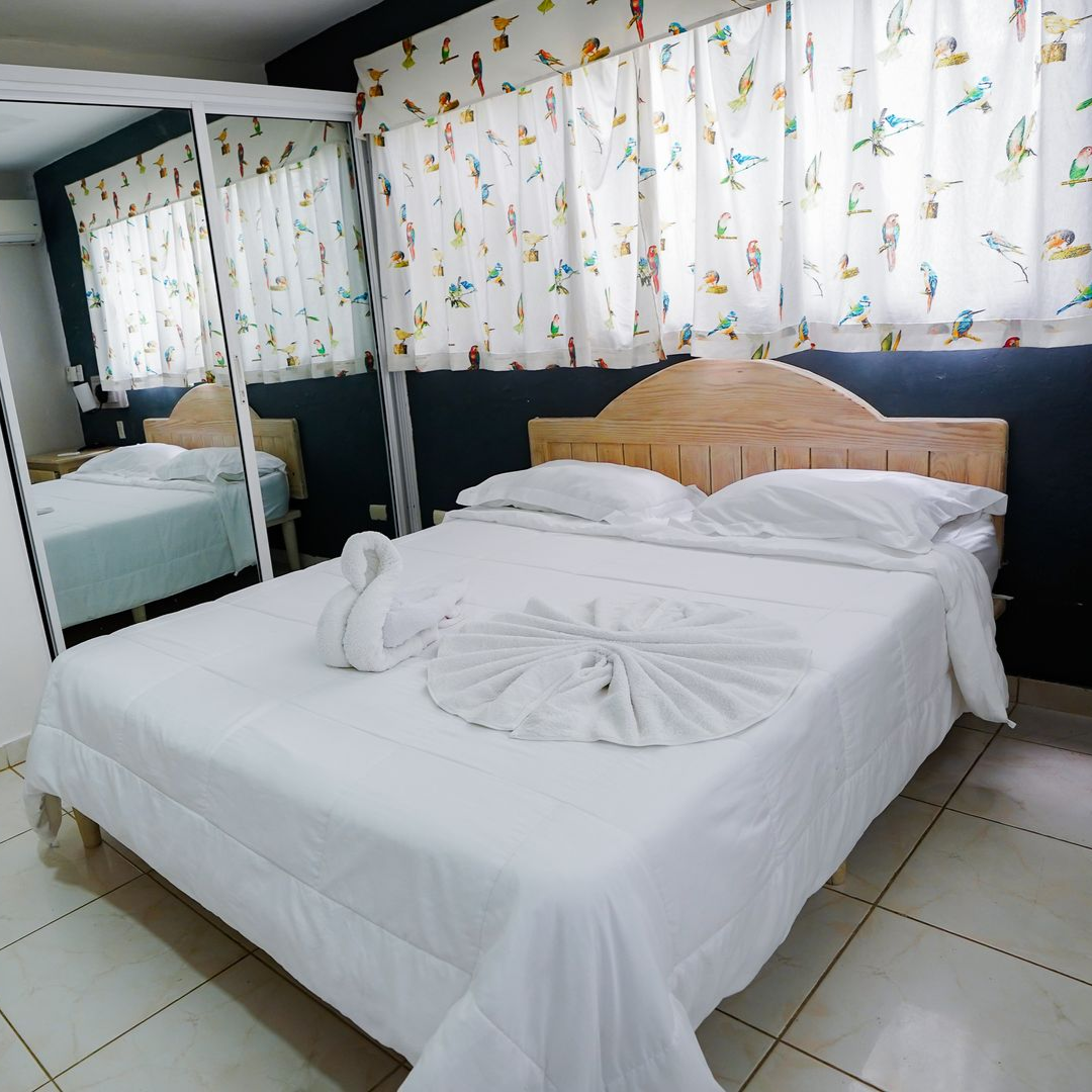 Bright bedroom with white bed linens, mirrored wardrobe, and patterned curtains