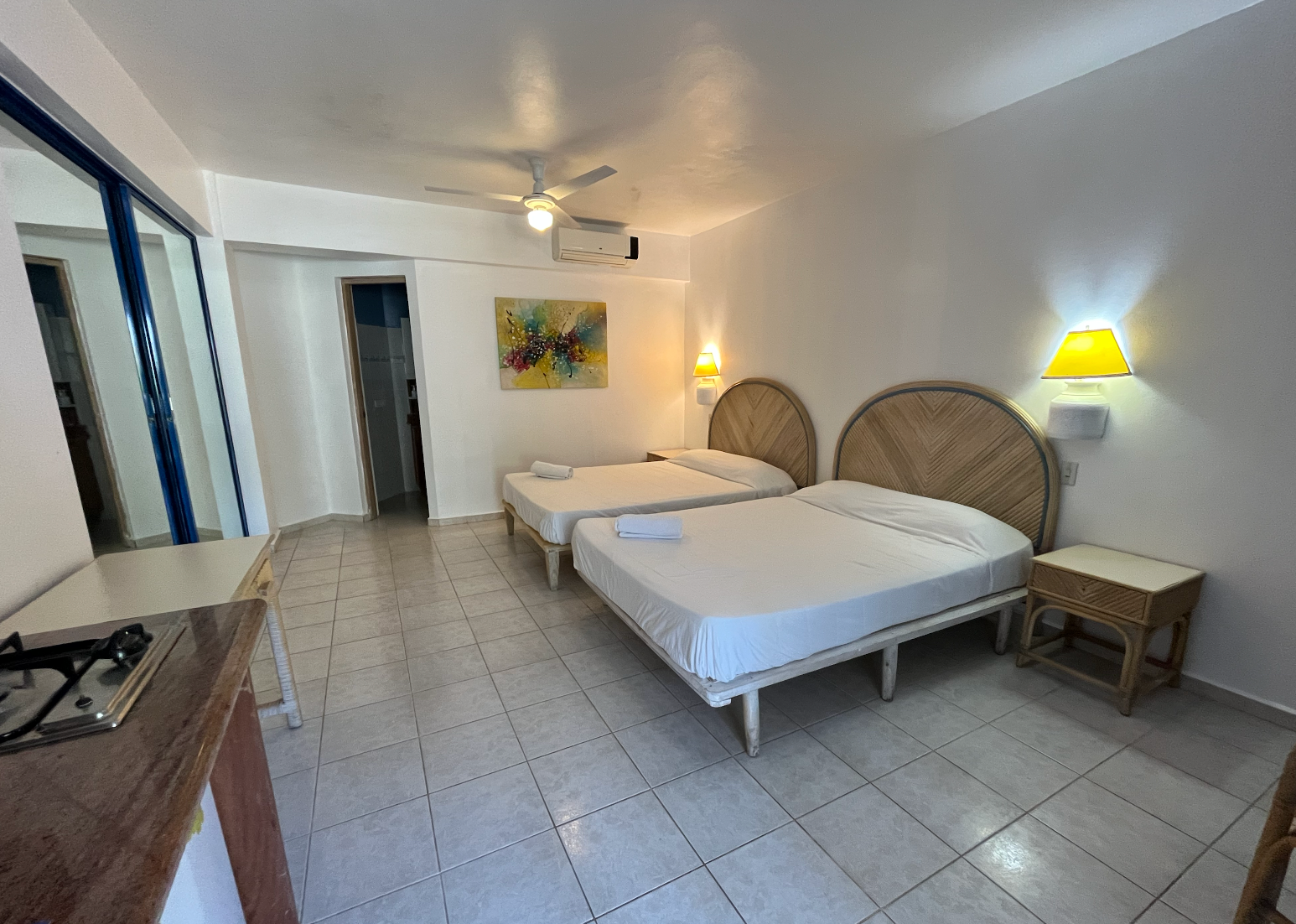 Spacious white bedroom with two twin beds, tiled floor, ceiling fan, and yellow bedside lamps.
