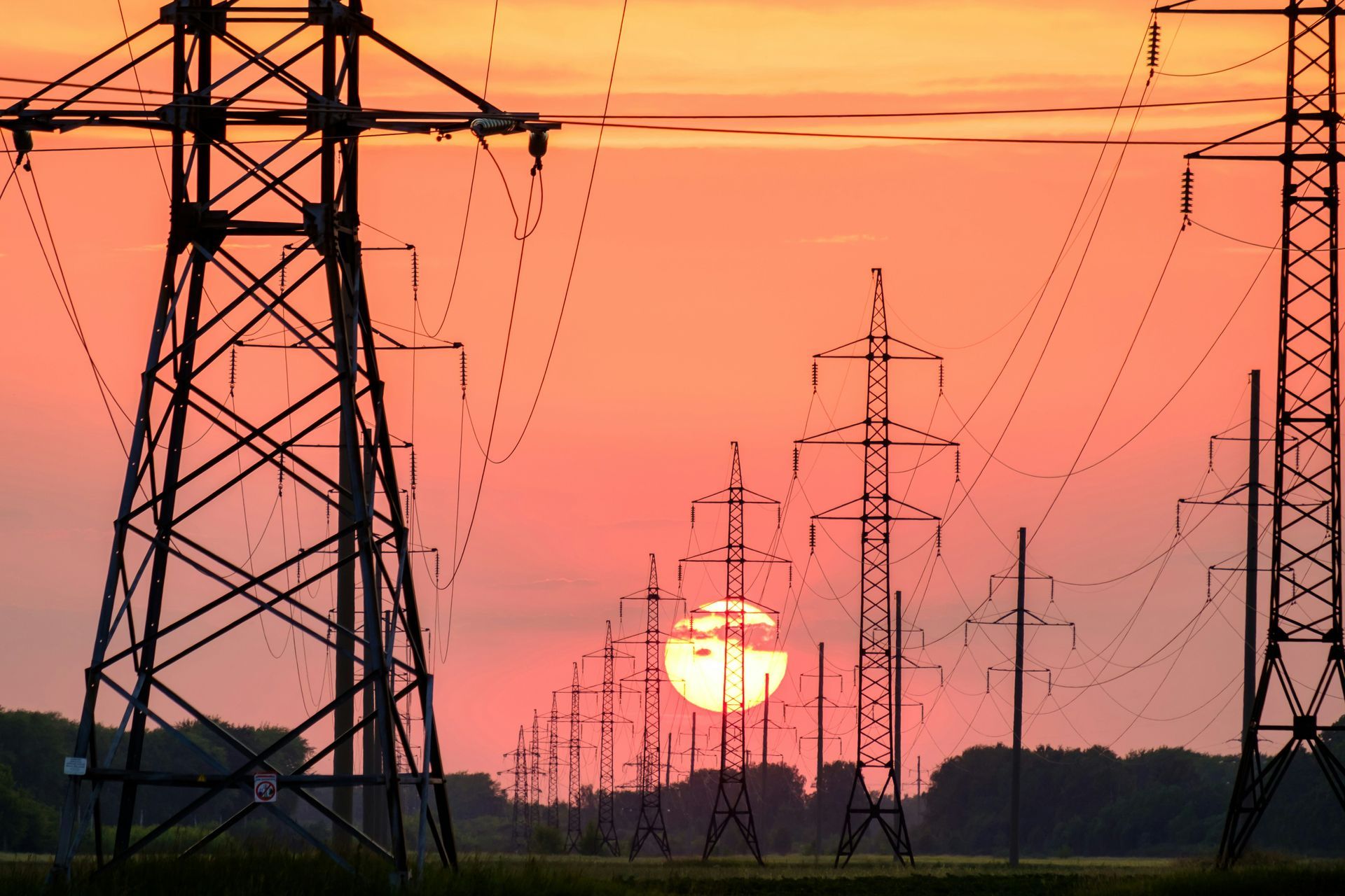 The sun is setting behind a row of power lines