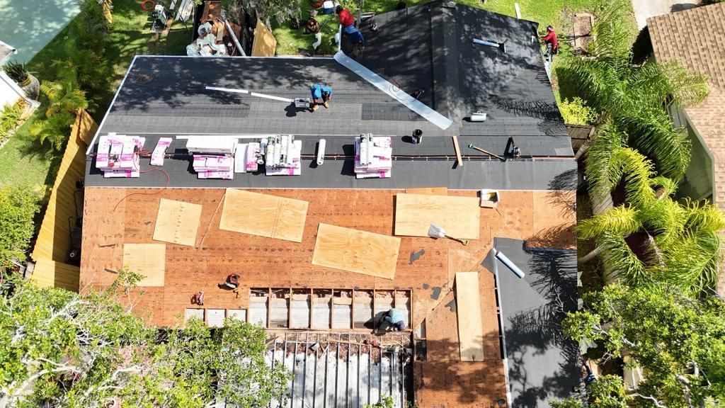 Aerial view of a house with laundry drying on the roof and a brick patio surrounded by greenery.