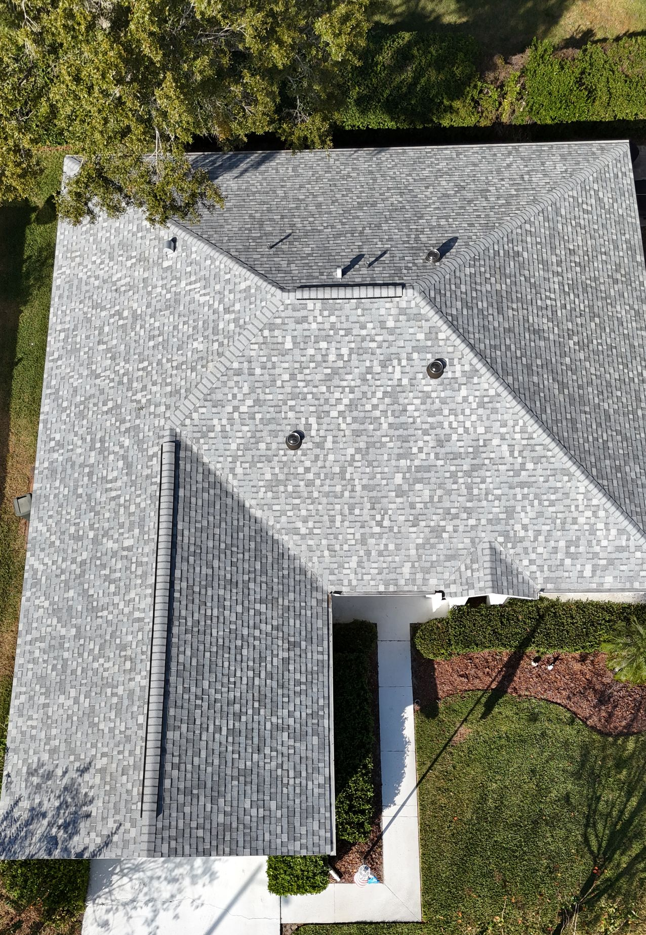 Aerial view of a gray-shingled house roof with a central white courtyard and surrounding trees and grass