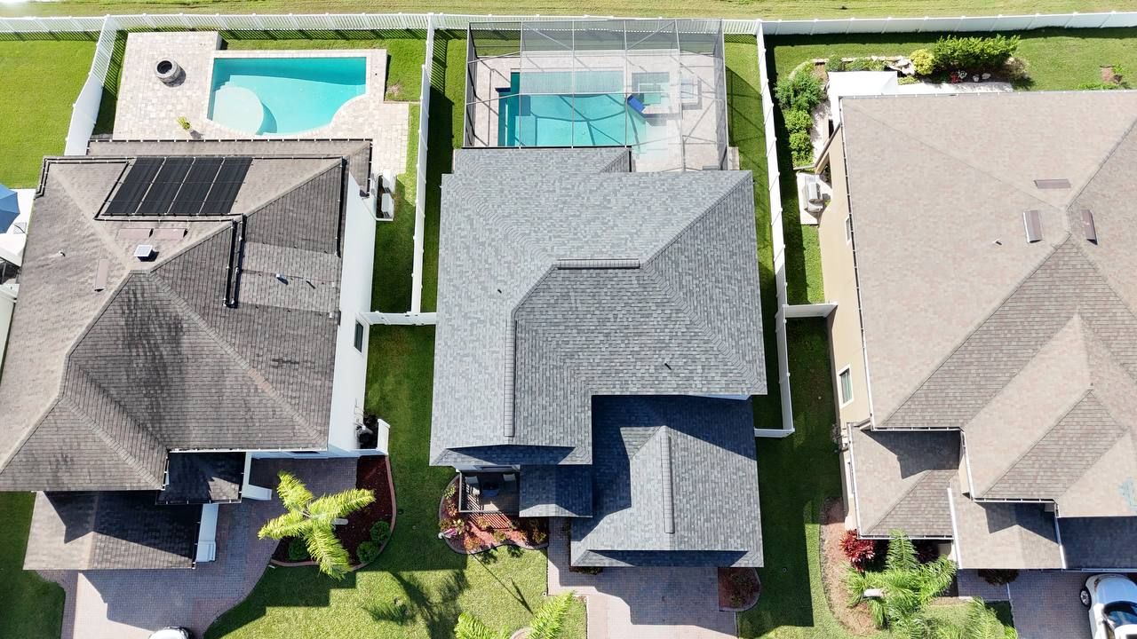 Aerial view of three houses with backyards and swimming pools, including solar panels on one roof.