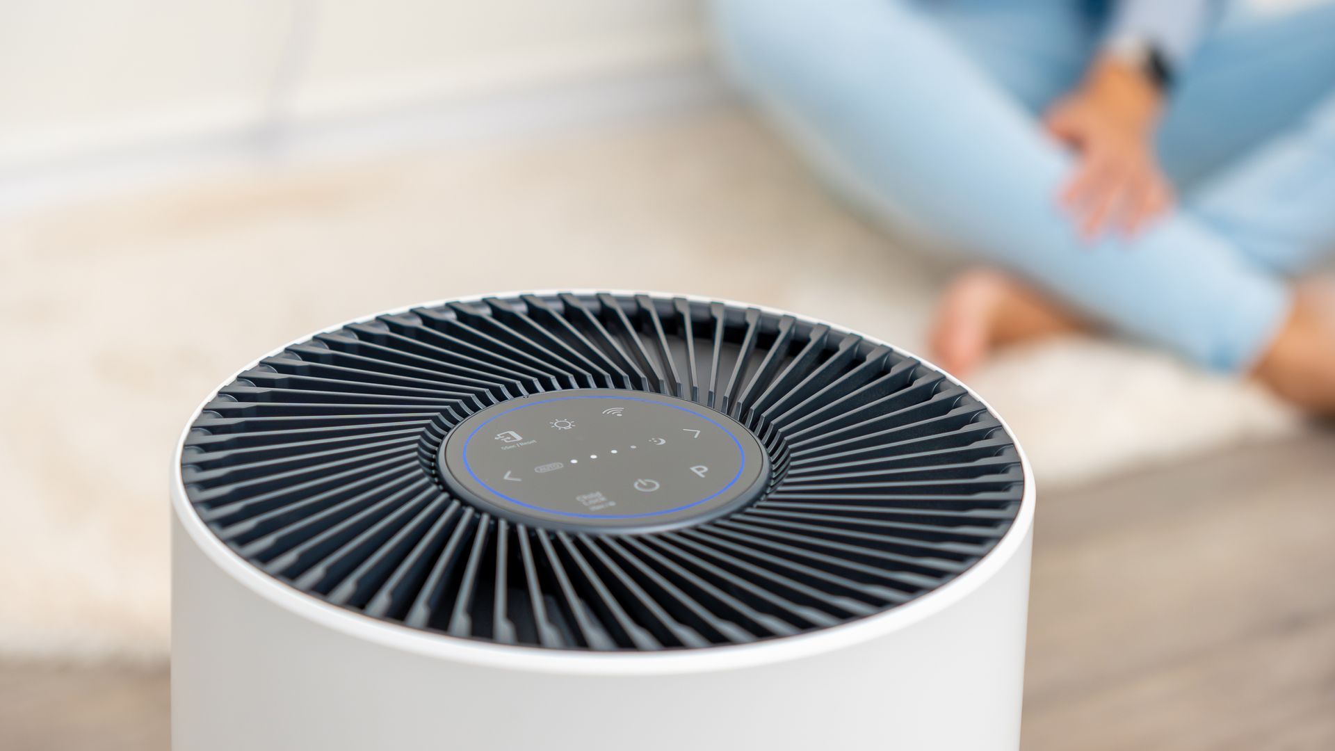 White air purifier with dark gray top, person in background.