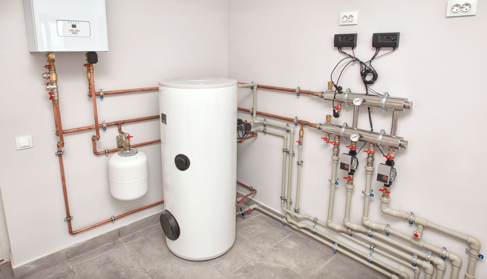 Heating system installation: boiler, hot water tank, pipes, and control panel in a utility room.