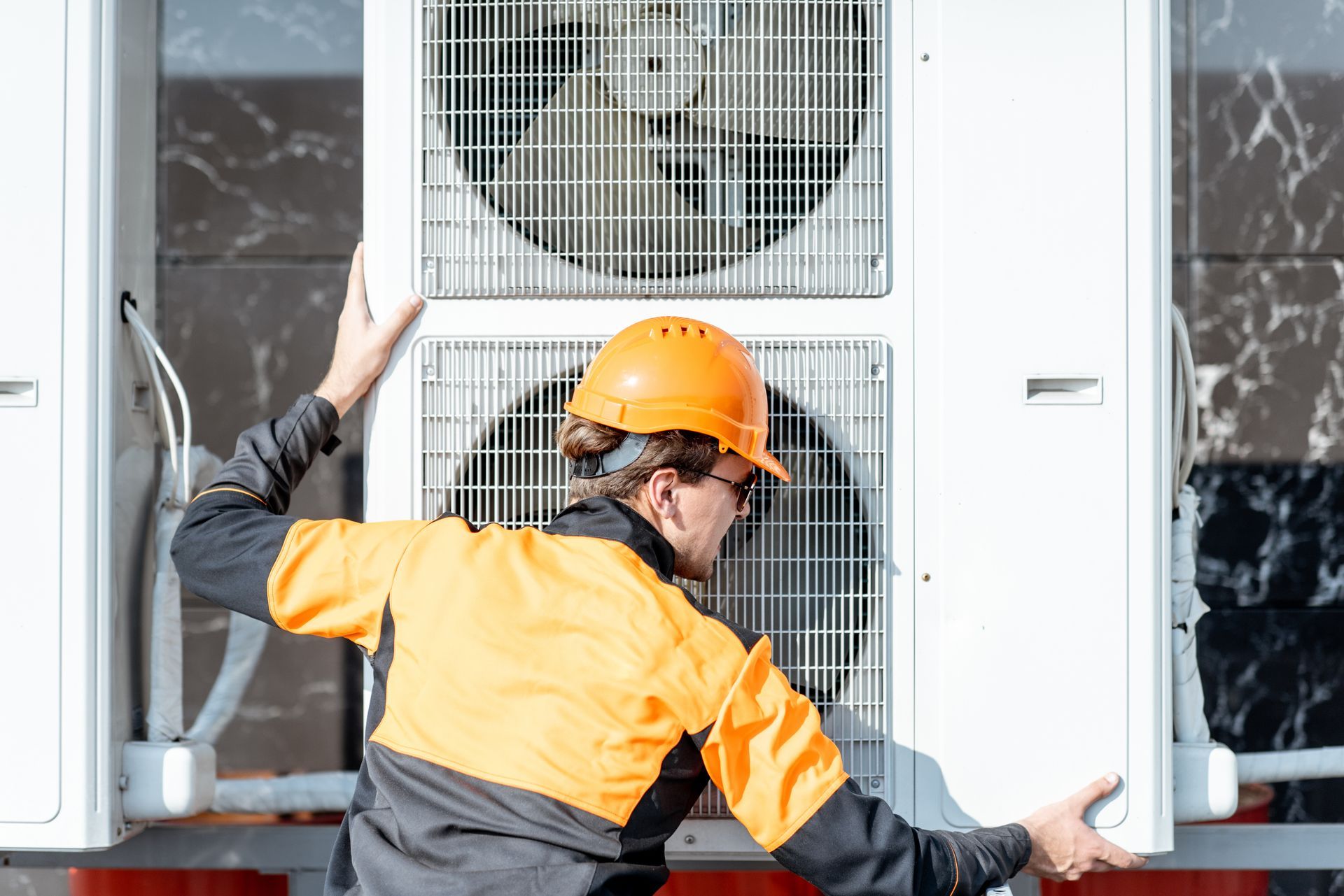Worker in orange safety gear installing an outdoor air conditioning unit.