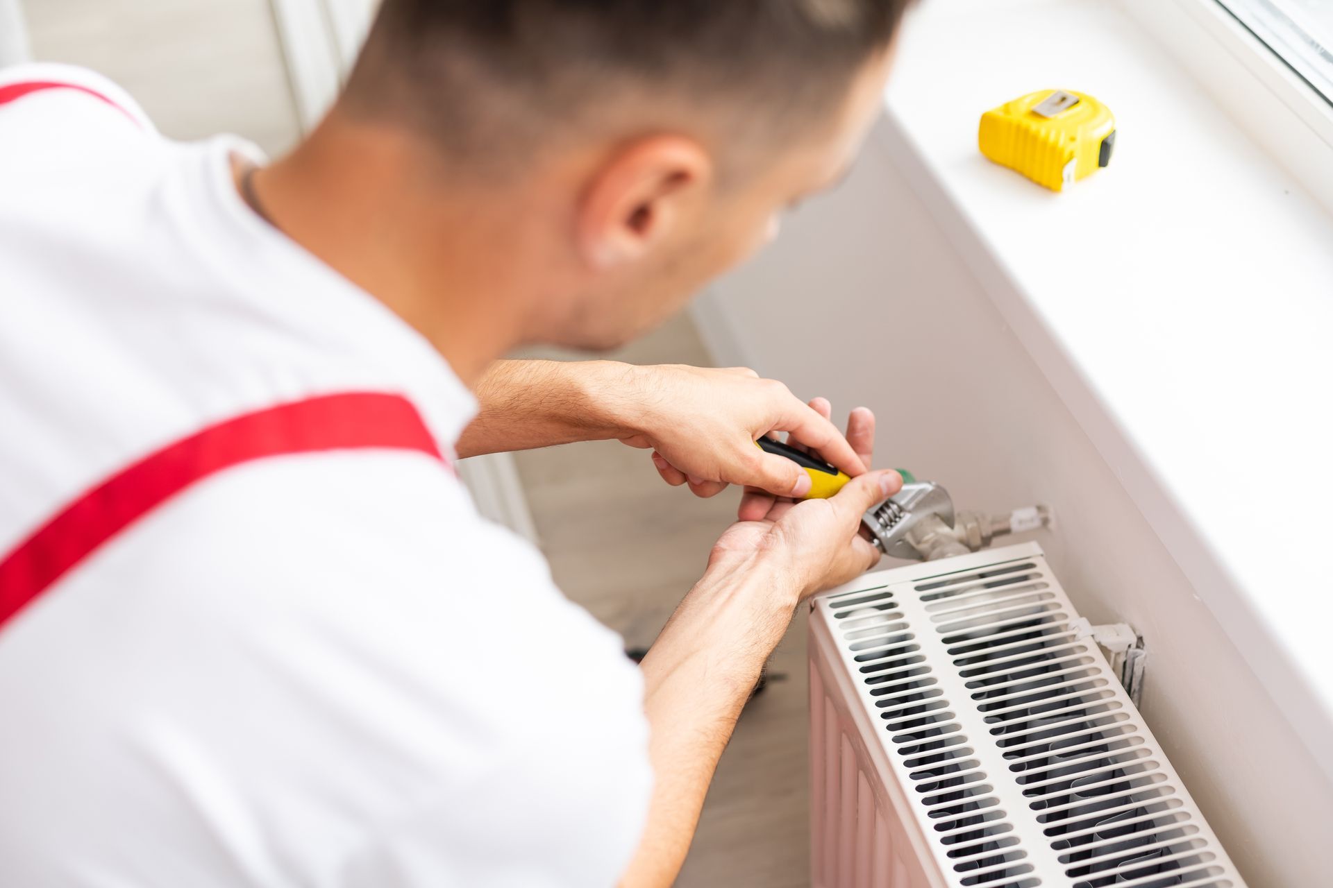 Person using a screwdriver to work on a radiator near a windowsill.