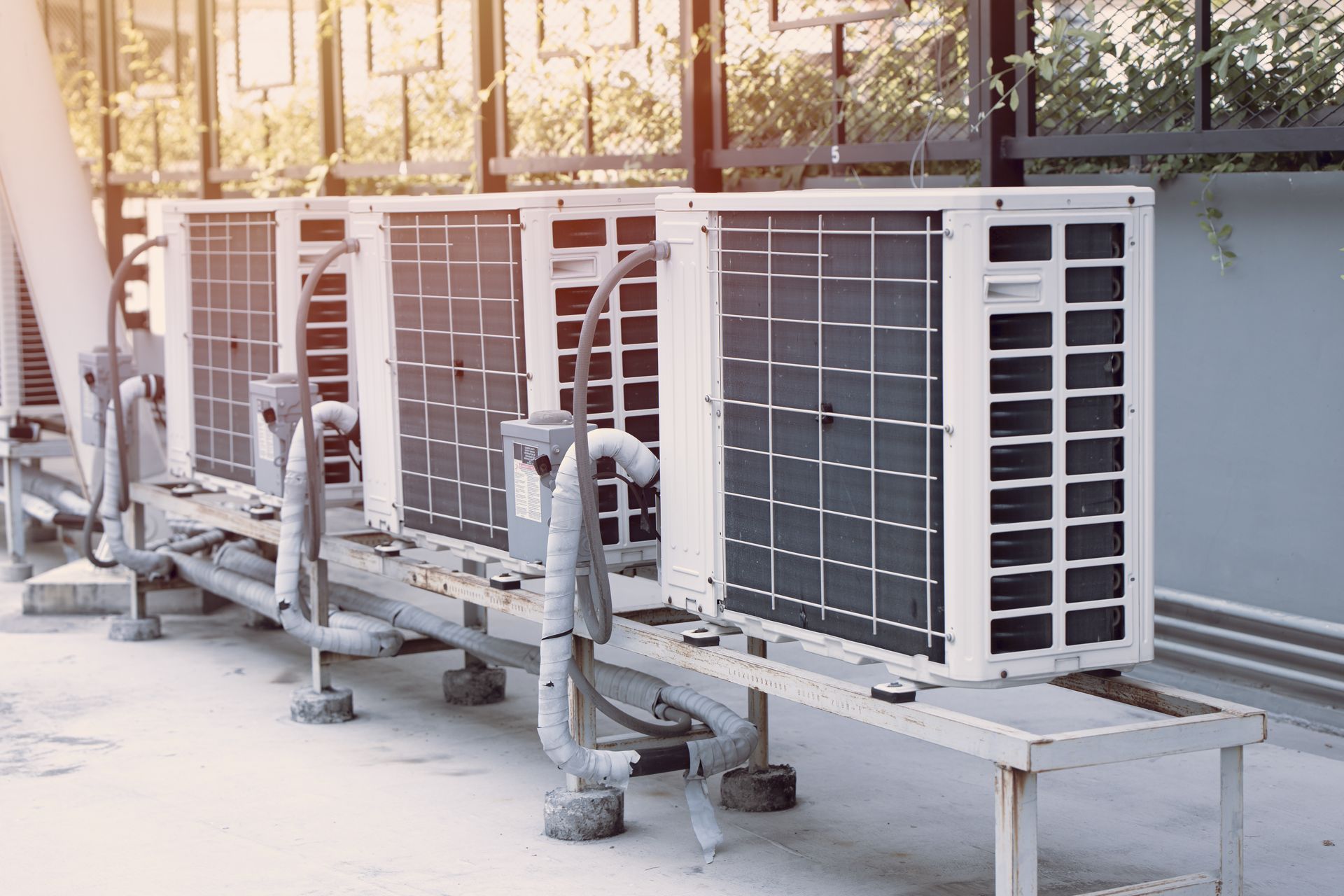 Outdoor air conditioning units lined up on a metal platform, with connected piping.