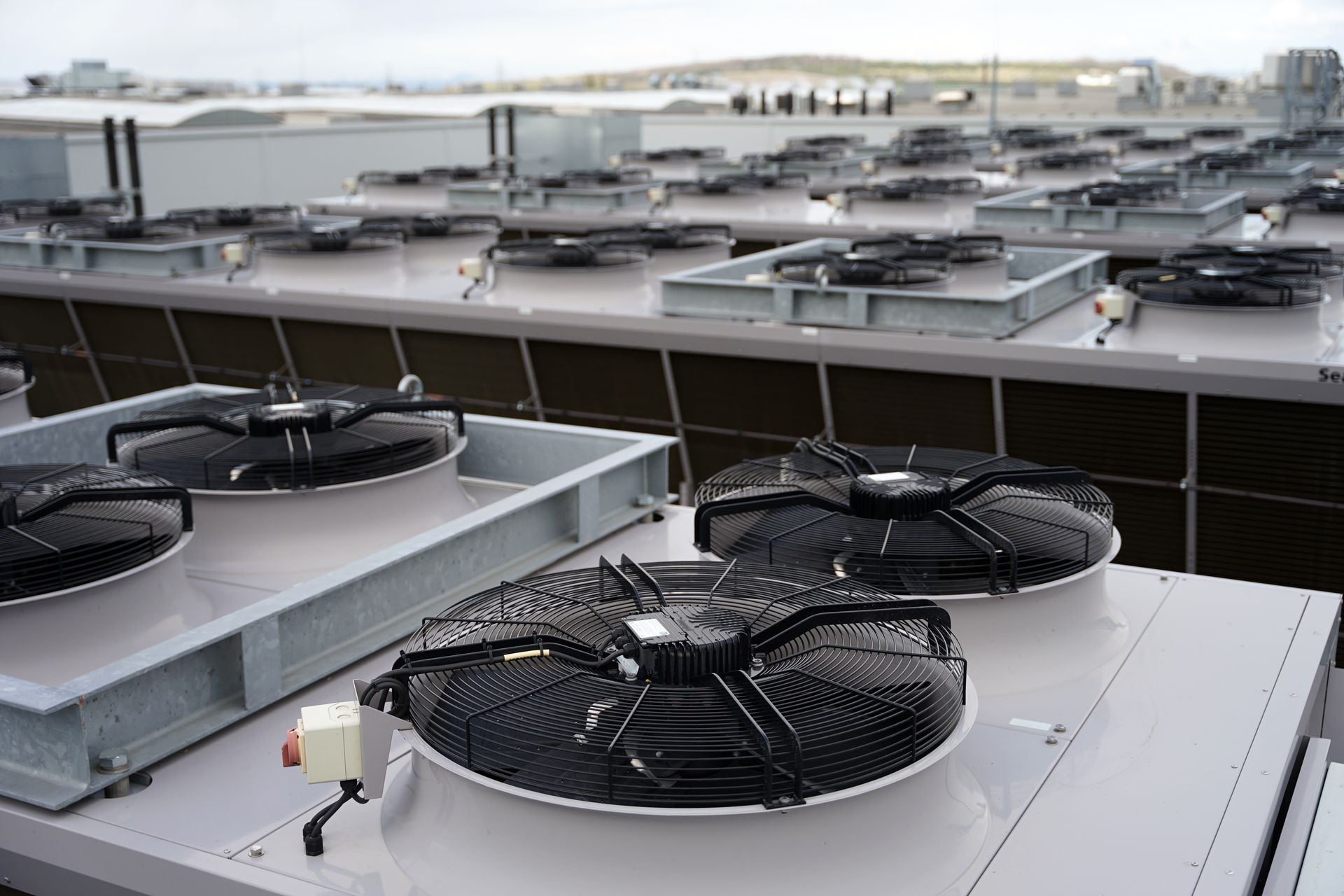 Rooftop view of several large industrial fans, likely for cooling, atop a building under a cloudy sky.