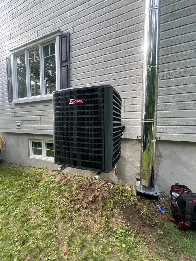 Un climatiseur noir est posé sur le côté d'une maison à côté d'une fenêtre.
