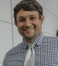A man wearing a plaid shirt and tie smiles for the camera