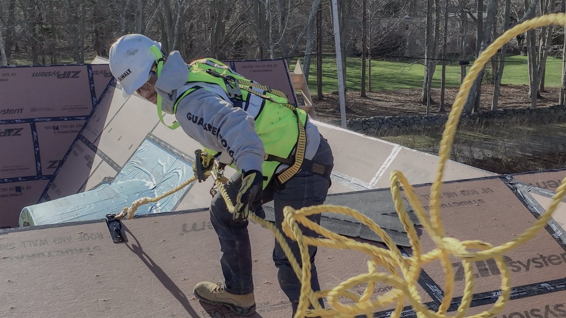 Roofer wearing safety gear, working on a roof. He’s pulling a rope.