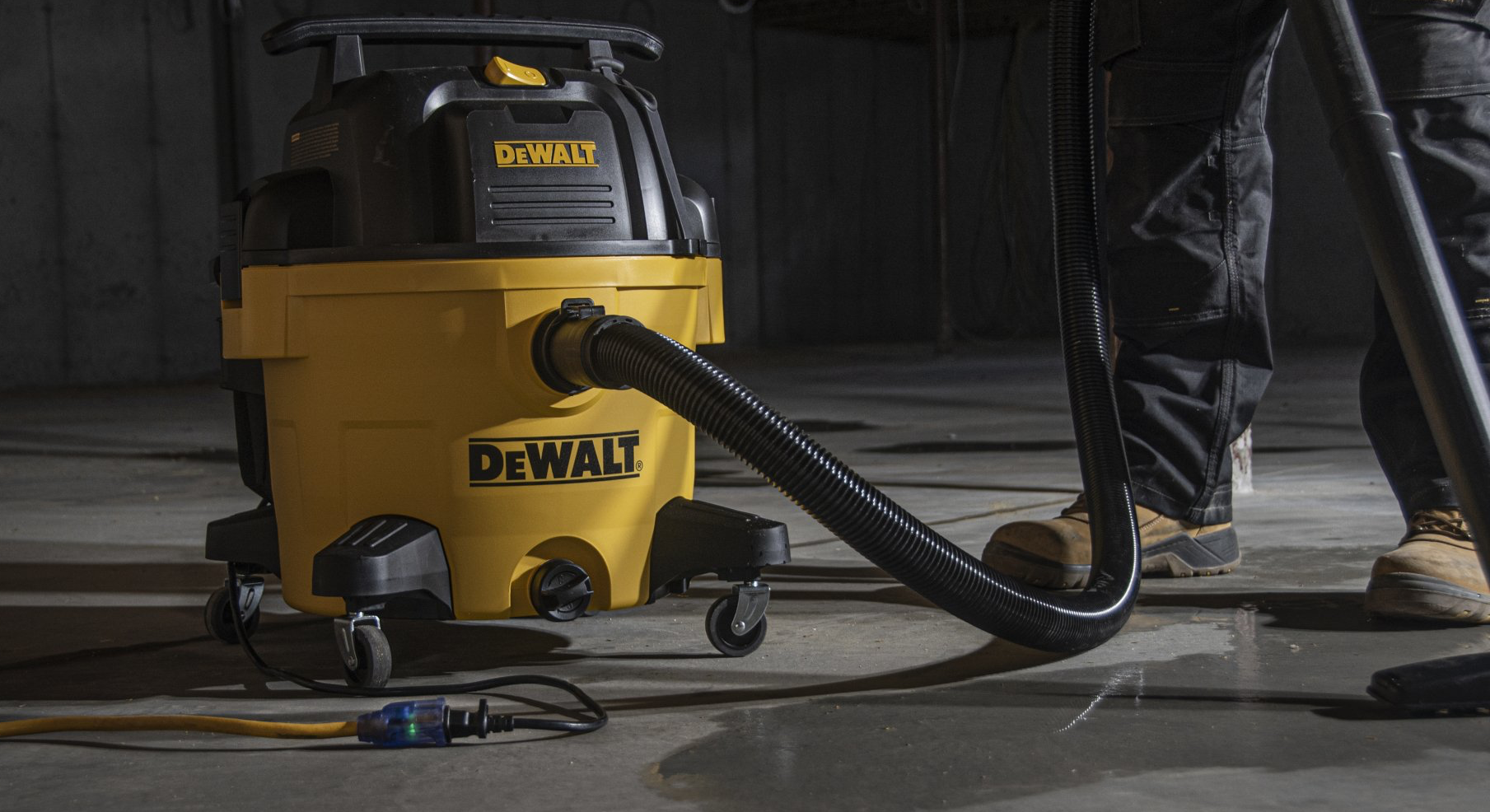 Yellow and black DeWalt wet/dry vacuum being used on a concrete floor in a dimly lit room.