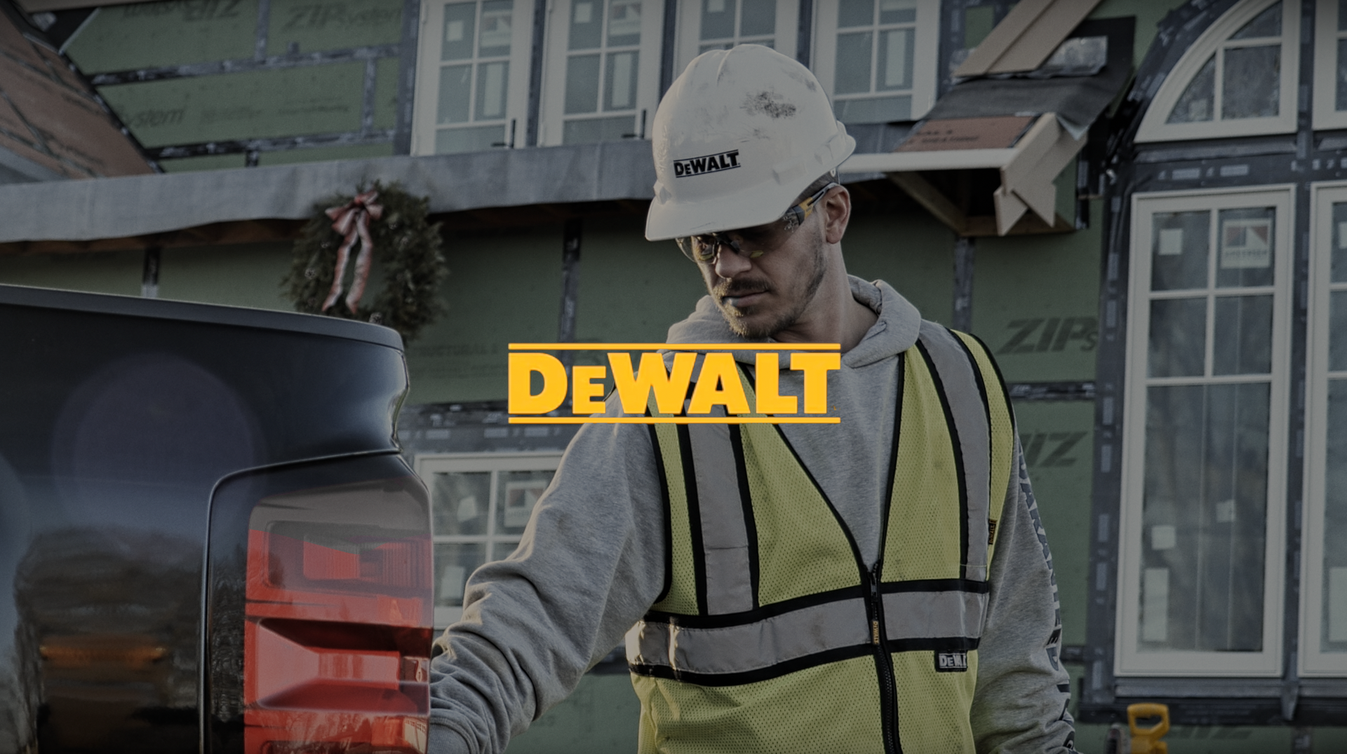 Man in hard hat and safety vest by a truck, working on a house, Dewalt logo.