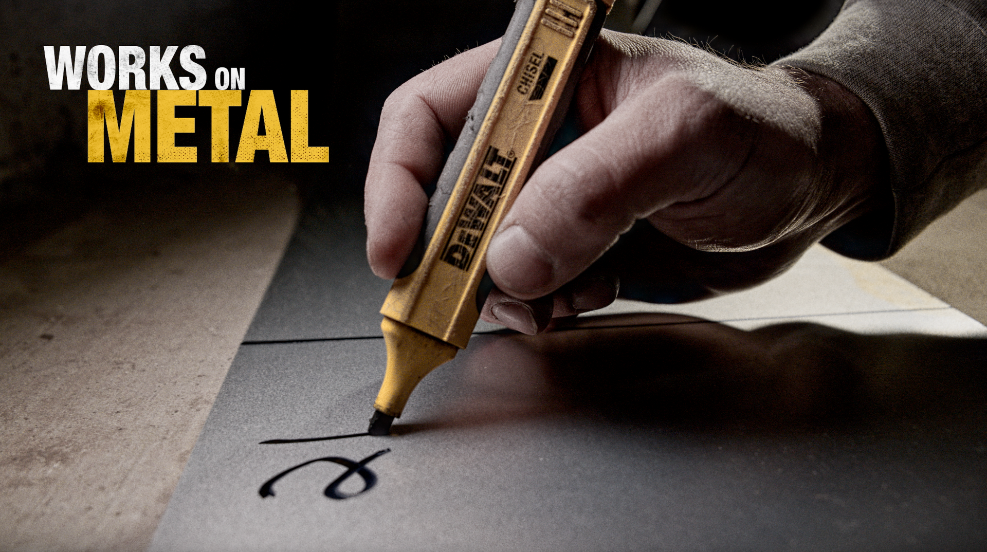 A hand holding a yellow marker writes on metal;