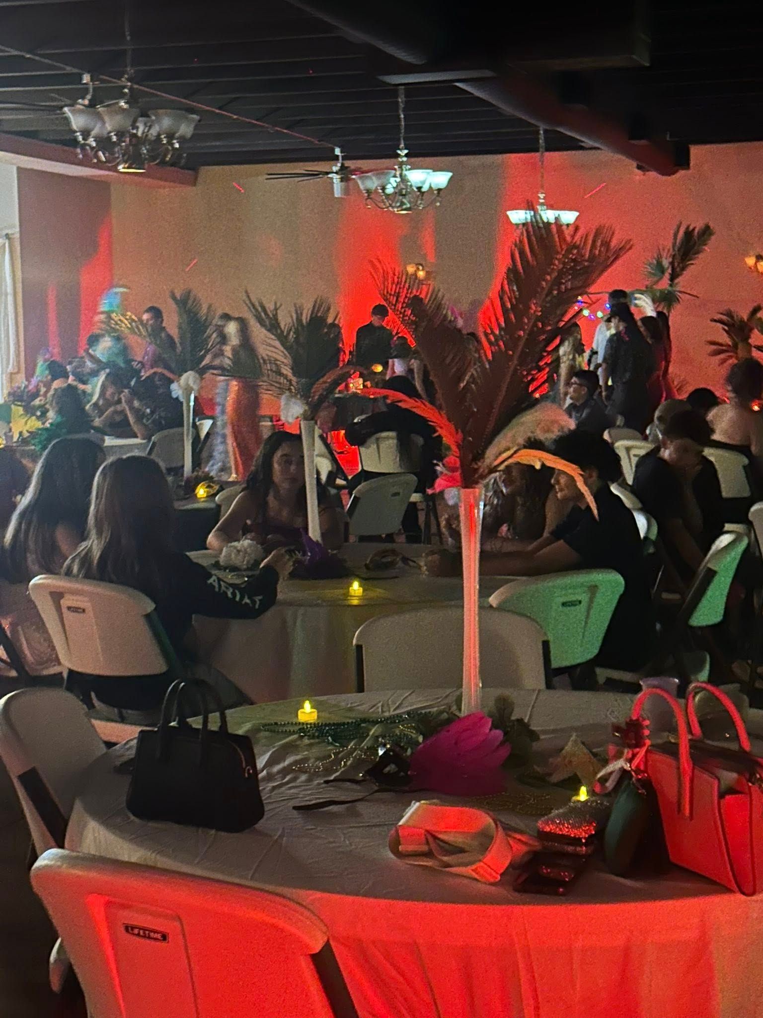 People at tables in a decorated event space with red lighting and centerpieces.