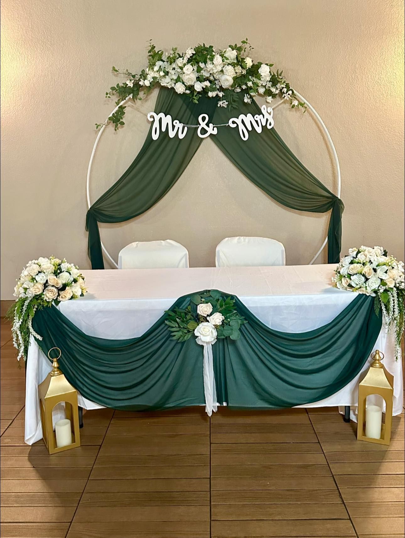 Wedding reception sweetheart table decorated with green and white floral arrangements.