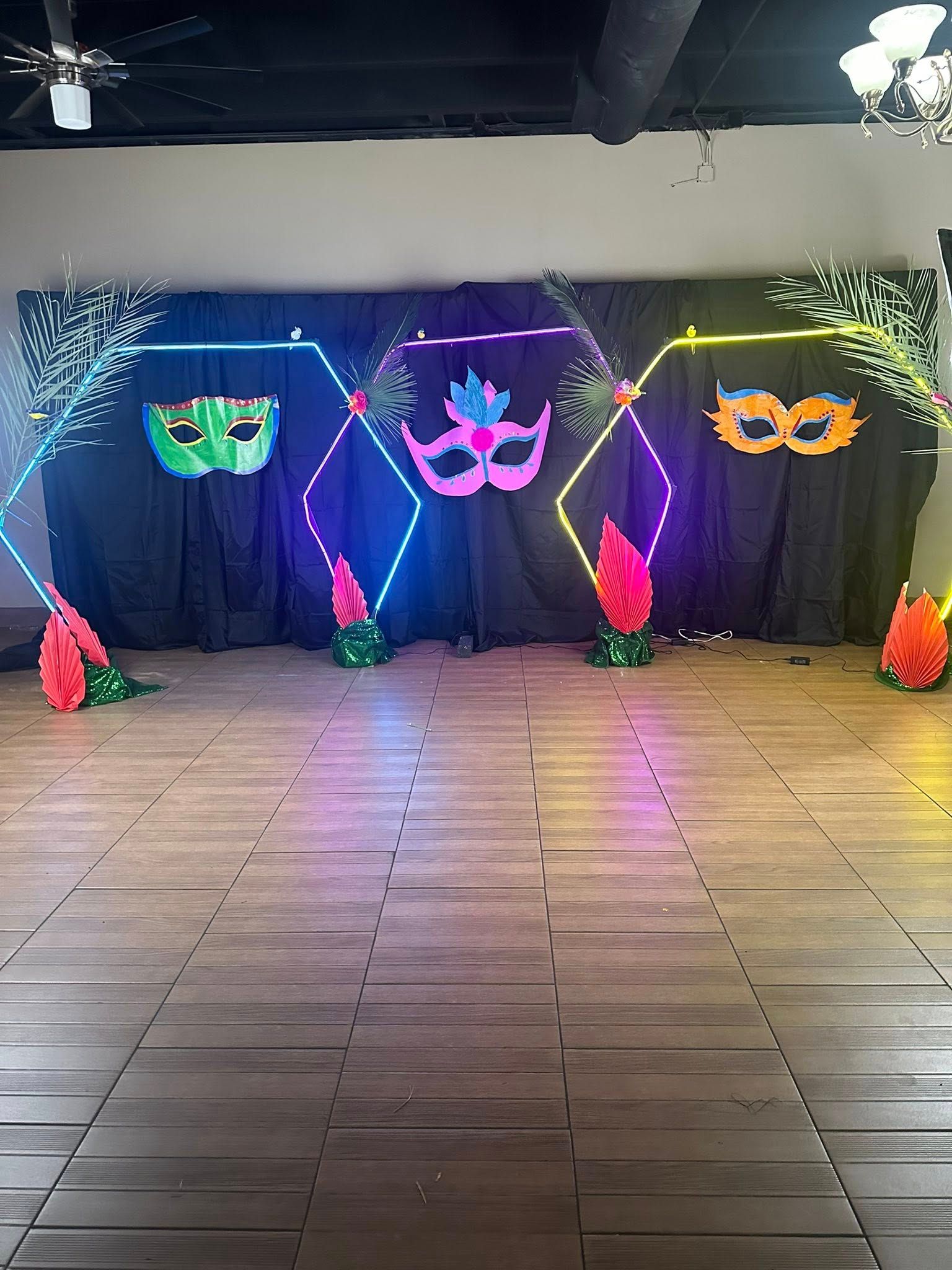 Mardi Gras-themed backdrop with masks, neon lights, and decorative floral elements on a wooden floor.