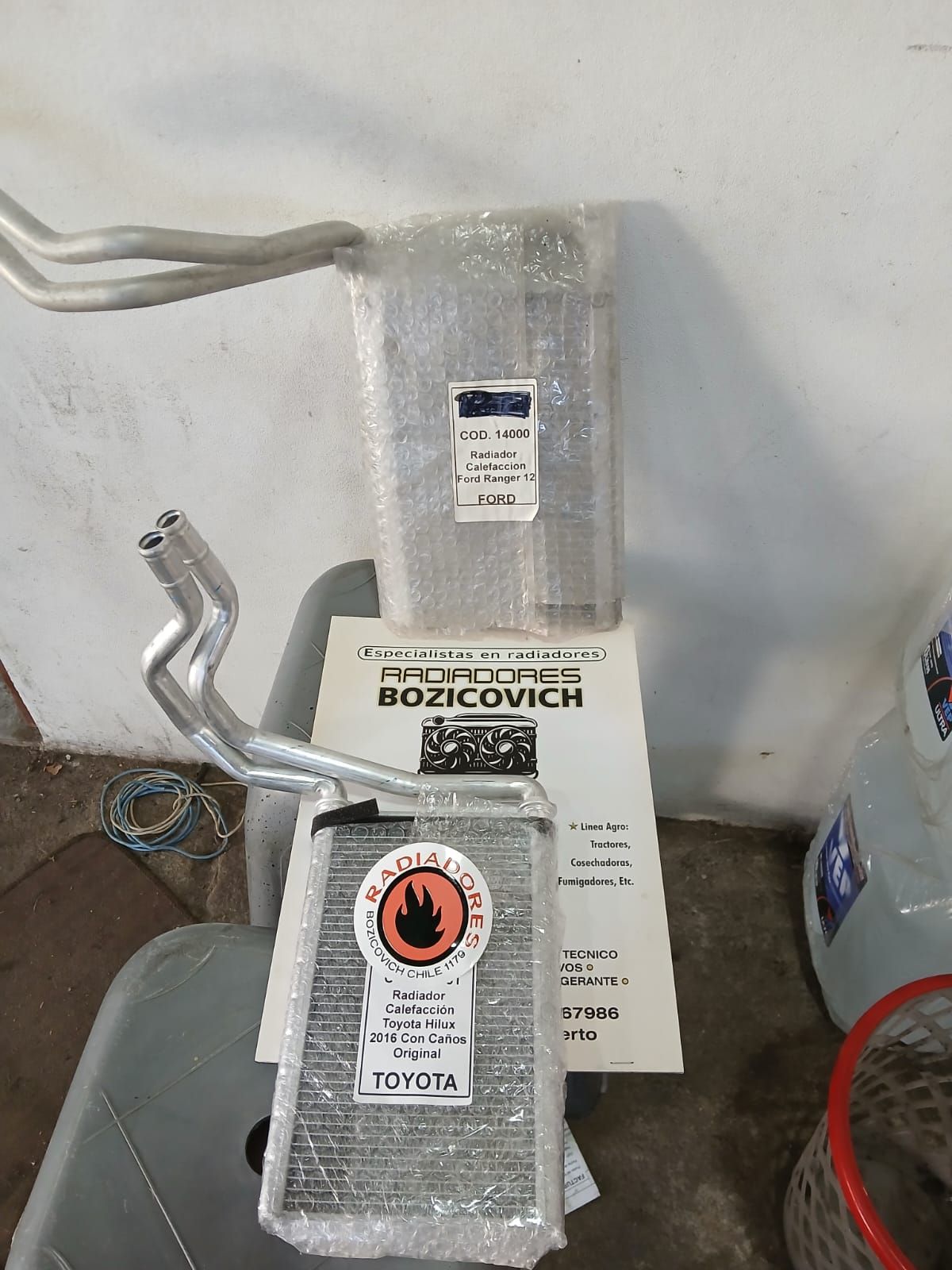 Unidad de climatización envuelta en papel de aluminio con una etiqueta, contra una pared blanca en un área de servicio.