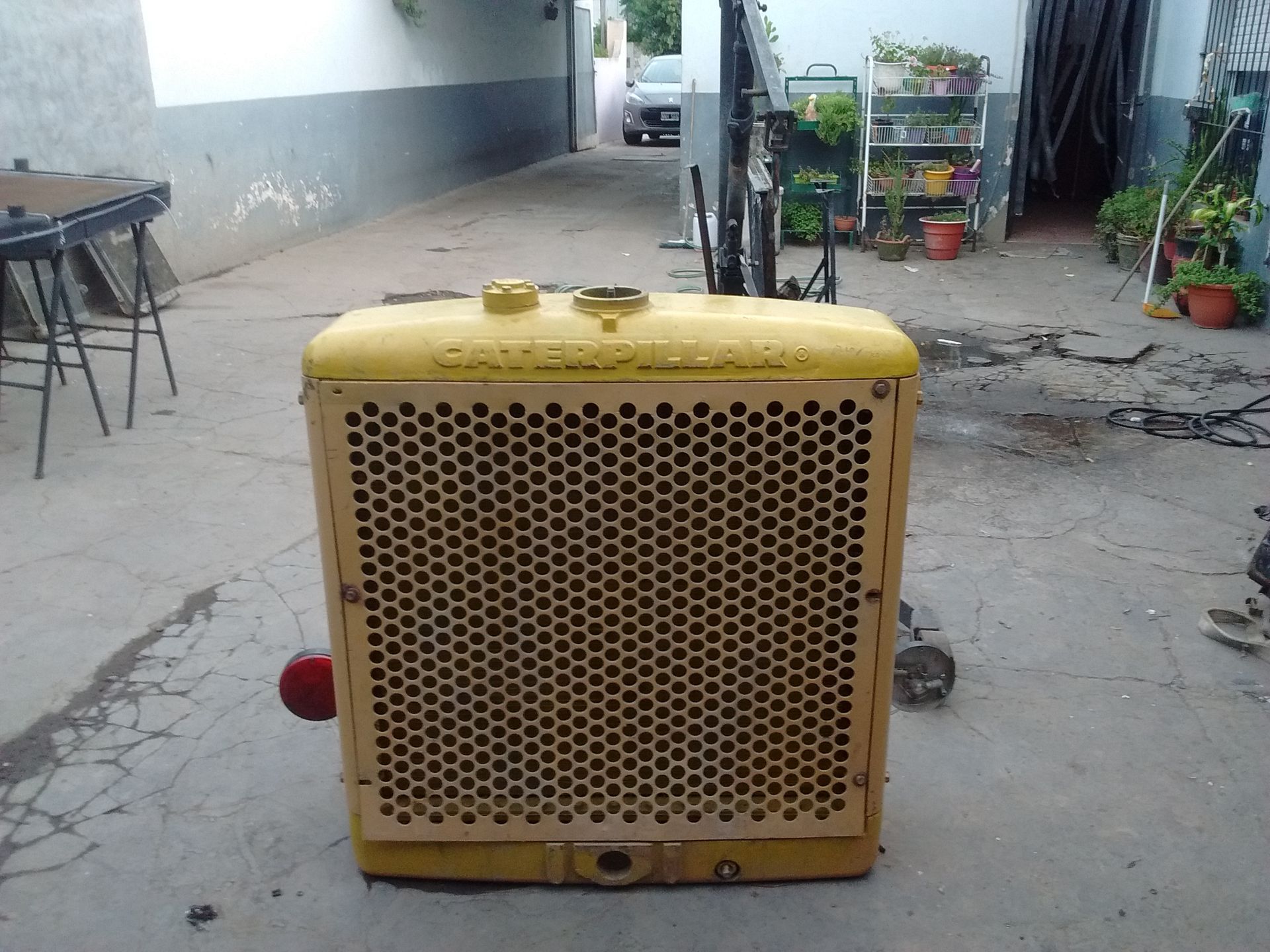 Rejilla frontal de metal amarillo de un pequeño electrodoméstico o máquina sobre un patio de concreto al aire libre.