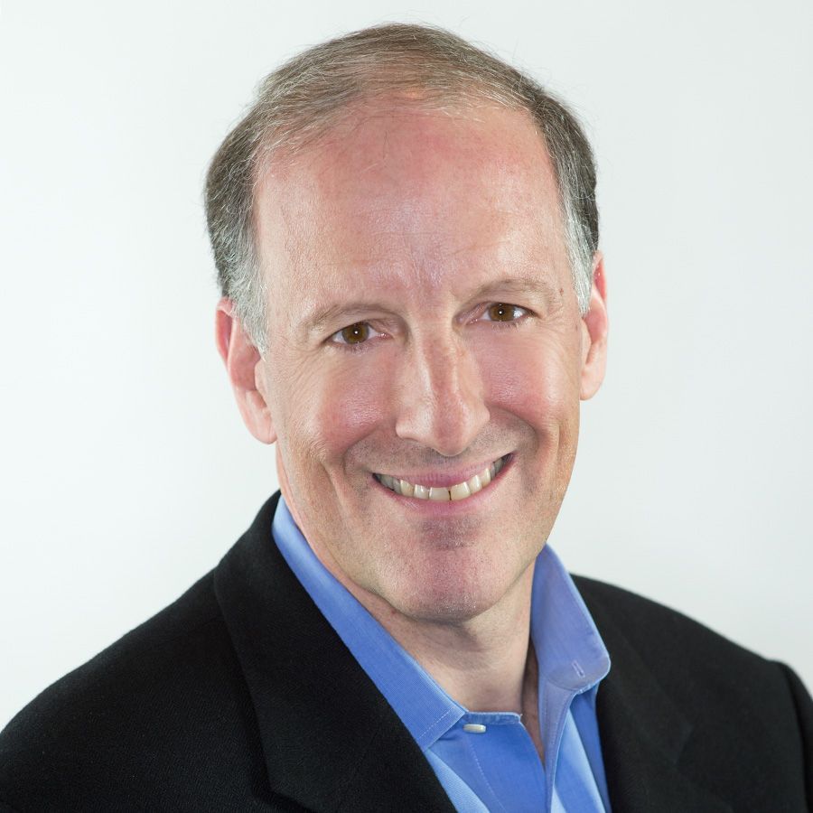 Smiling man with fair skin in a blue shirt and black blazer.