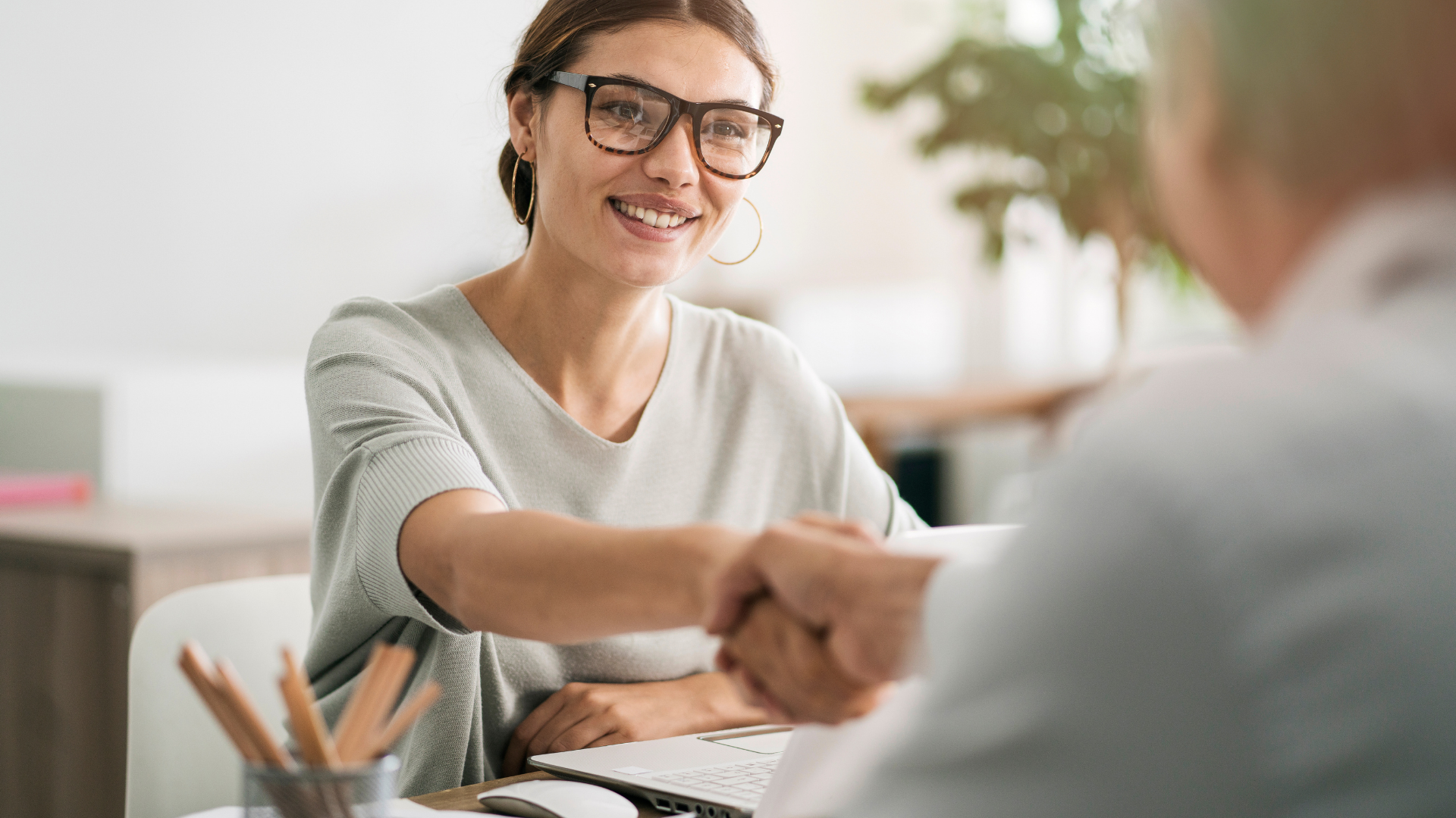 Smiling woman shaking hands across a desk in a bright office setting