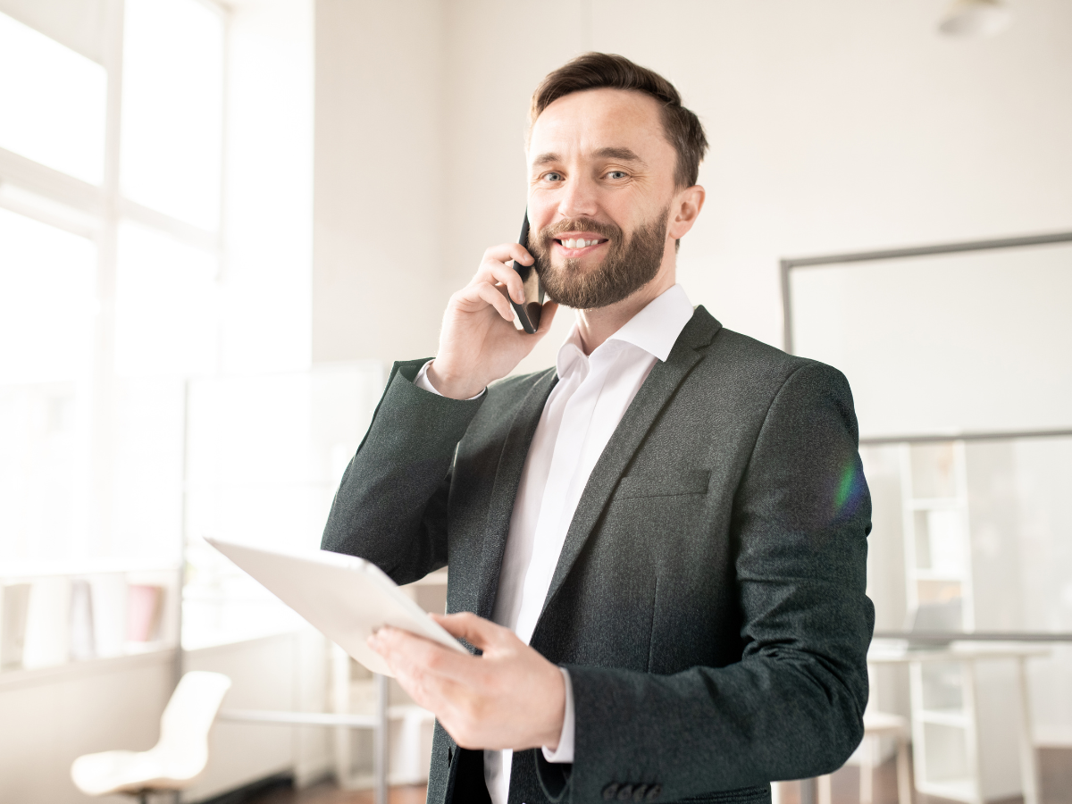 Man in suit, smiling, on phone while holding tablet in office.