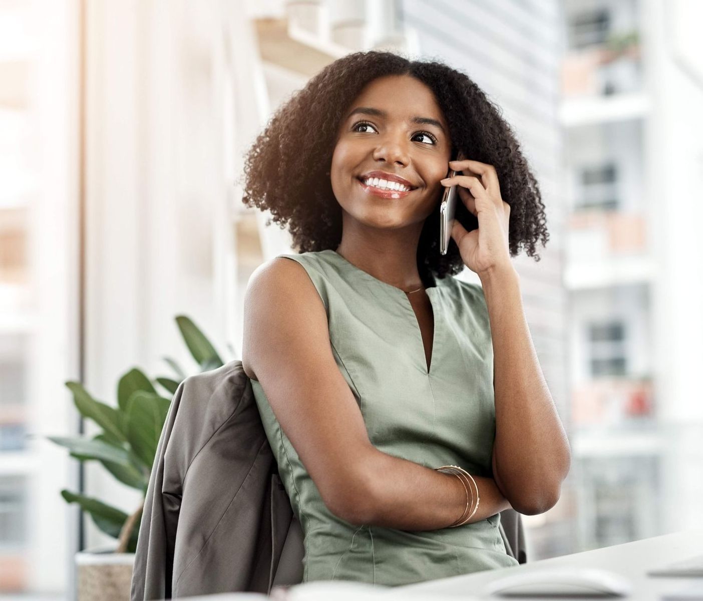 Woman with curly hair, smiling while talking on a cell phone in an office setting.