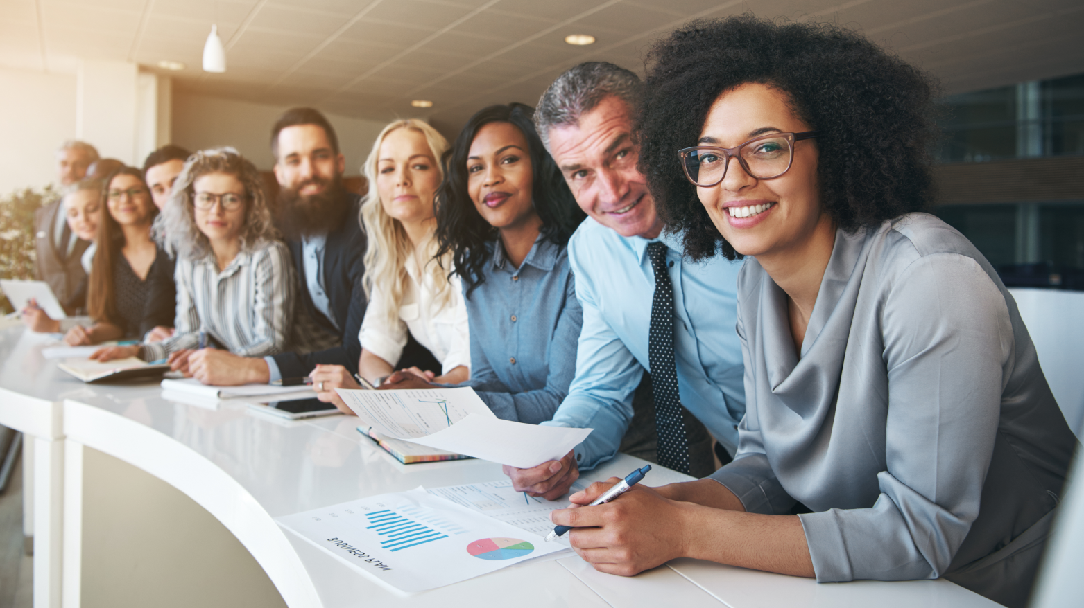 Group of diverse business people smiling at a conference table, reviewing documents.