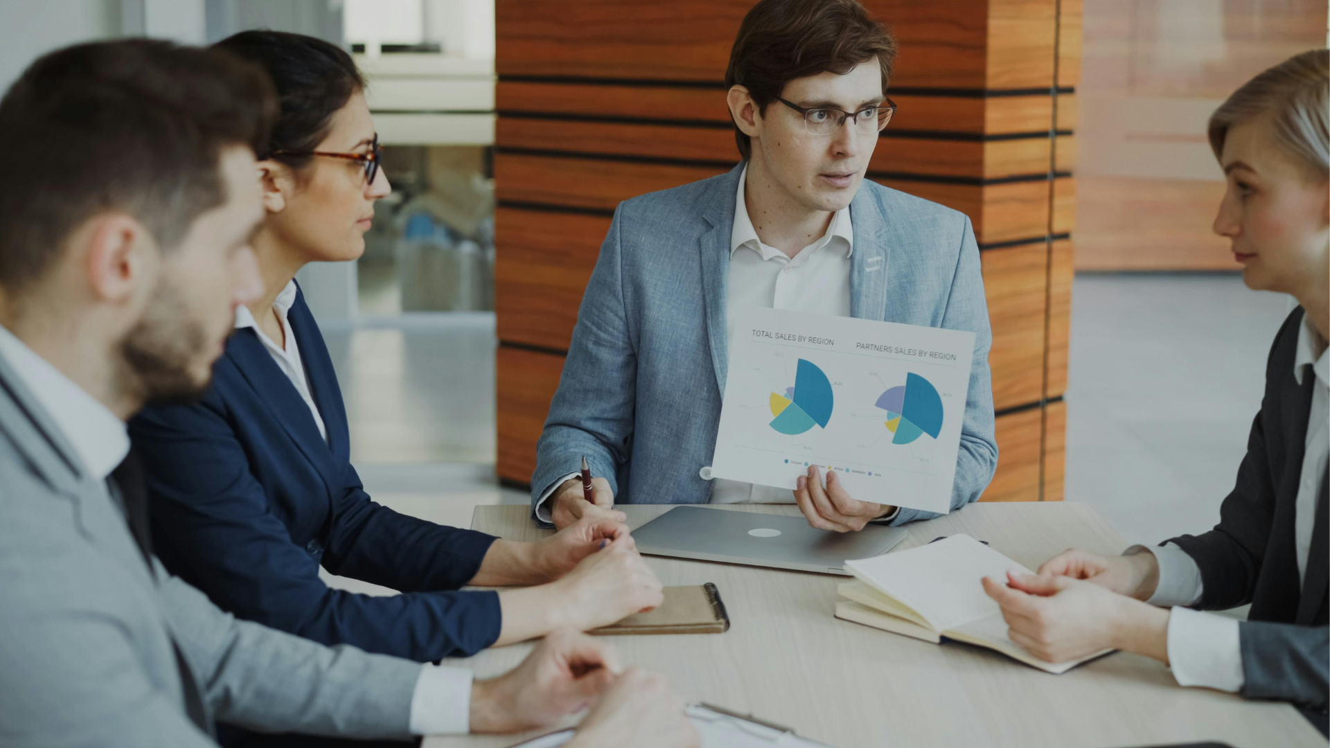 Business team in a meeting, with a man presenting colorful charts at a conference table.