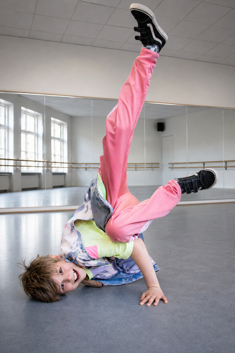 Een danseres in een roze outfit balanceert ondersteboven in een studio met een spiegelwand.