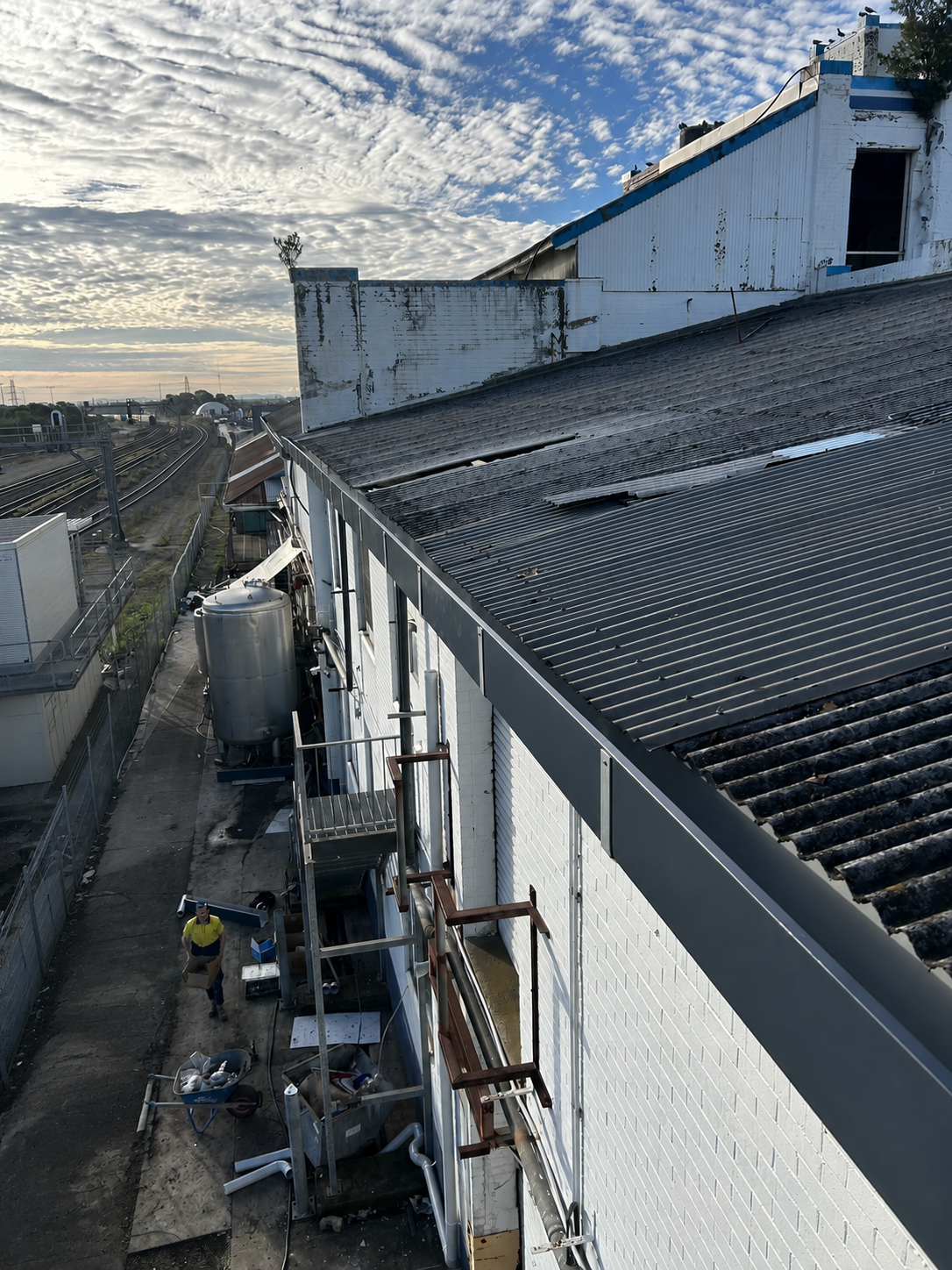 Roofline and gutter on a building, with scaffolding along the side under a cloudy sky.  — Huddo's Plumbing Service in Wallalong, NSW