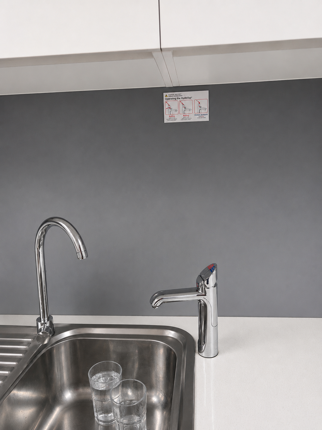 Kitchen Sink With Cleaning Supplies, Faucet, and Dishes Under a Reflective Backsplash — Huddo's Plumbing Service in Hunter Valley, NSW