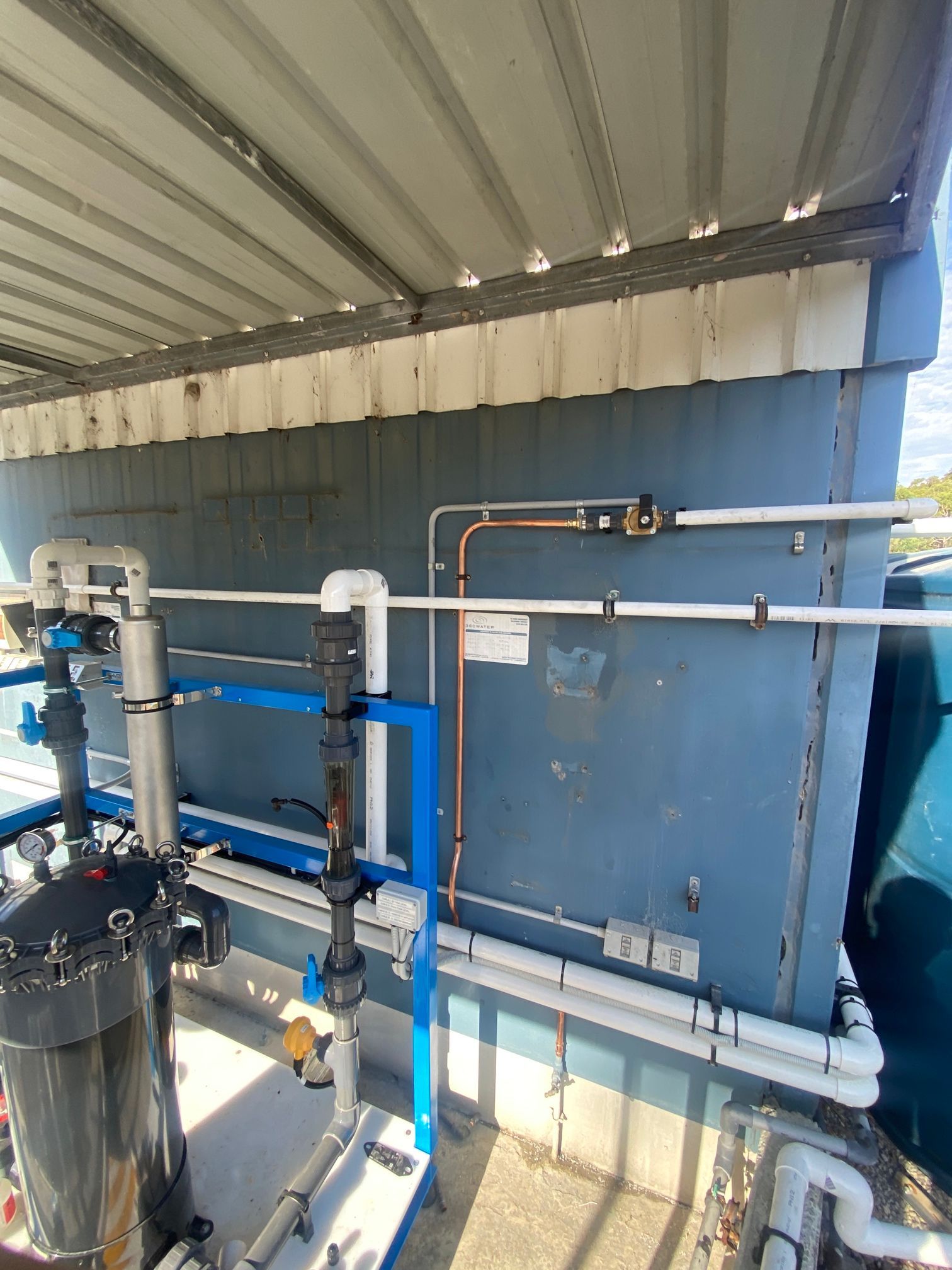 Industrial Pipes and Tanks Under a Corrugated Metal Roof — Huddo's Plumbing Service in Port Stephens, NSW