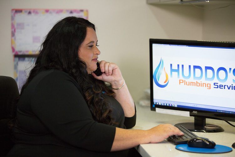 Woman At A Desk On The Phone, Using A Computer — Huddo's Plumbing Service in Wallalong, NSW
