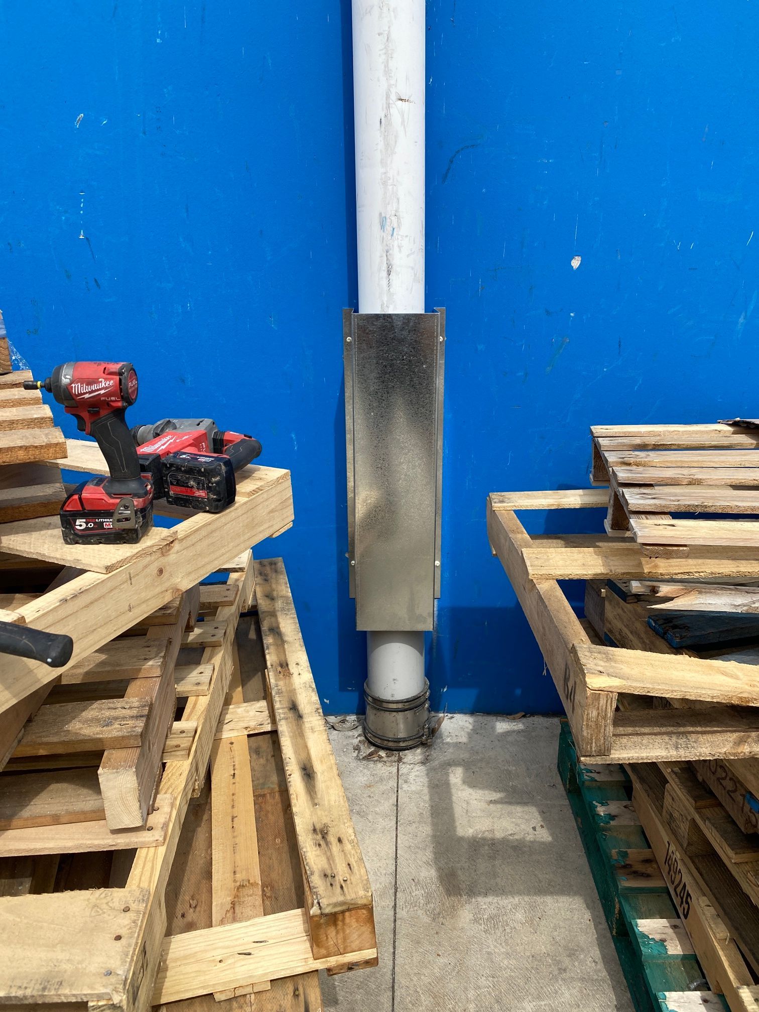 Blue Wall With Stacked Wooden Pallets and a Red Power Drill — Huddo's Plumbing Service in Newcastle, NSW
