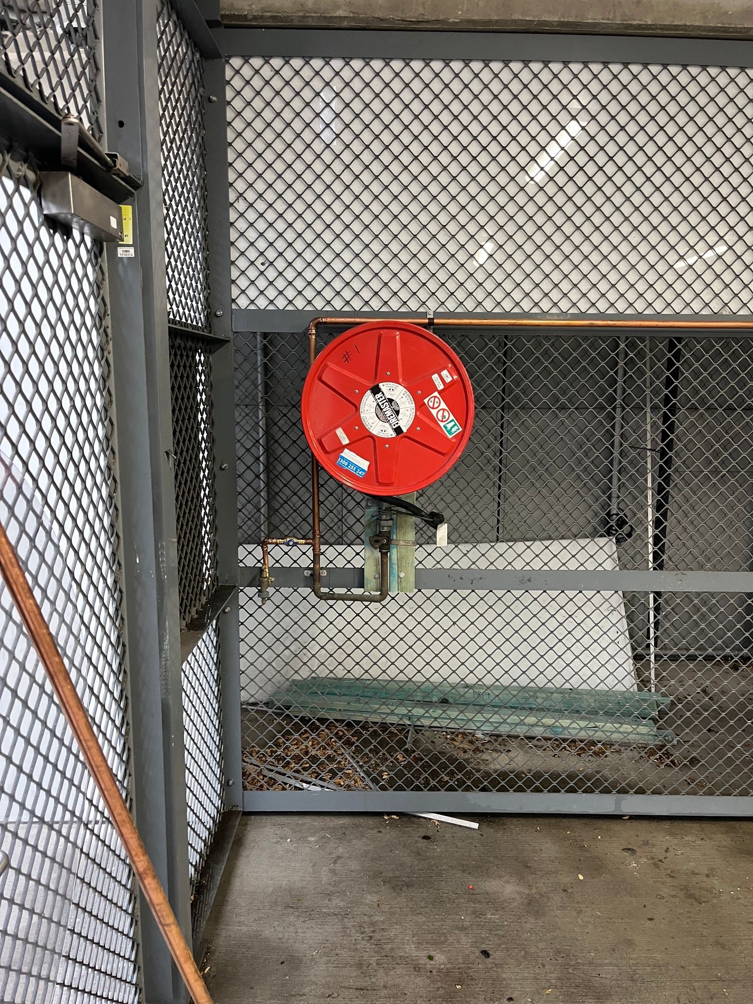 Red Fire Hose Reel Mounted on a Wall Inside a Chain-link — Huddo's Plumbing Service in Wallalong, NSW