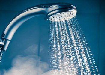 Chrome Showerhead Spraying Water Against A Blue Background — Huddo's Plumbing Service in Wallalong, NSW