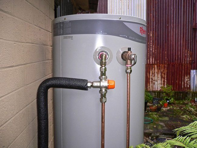 Outdoor Water Heater With Copper Pipes And A Black Insulated Hose Beside A Wall — Huddo's Plumbing Service in Wallalong, NSW