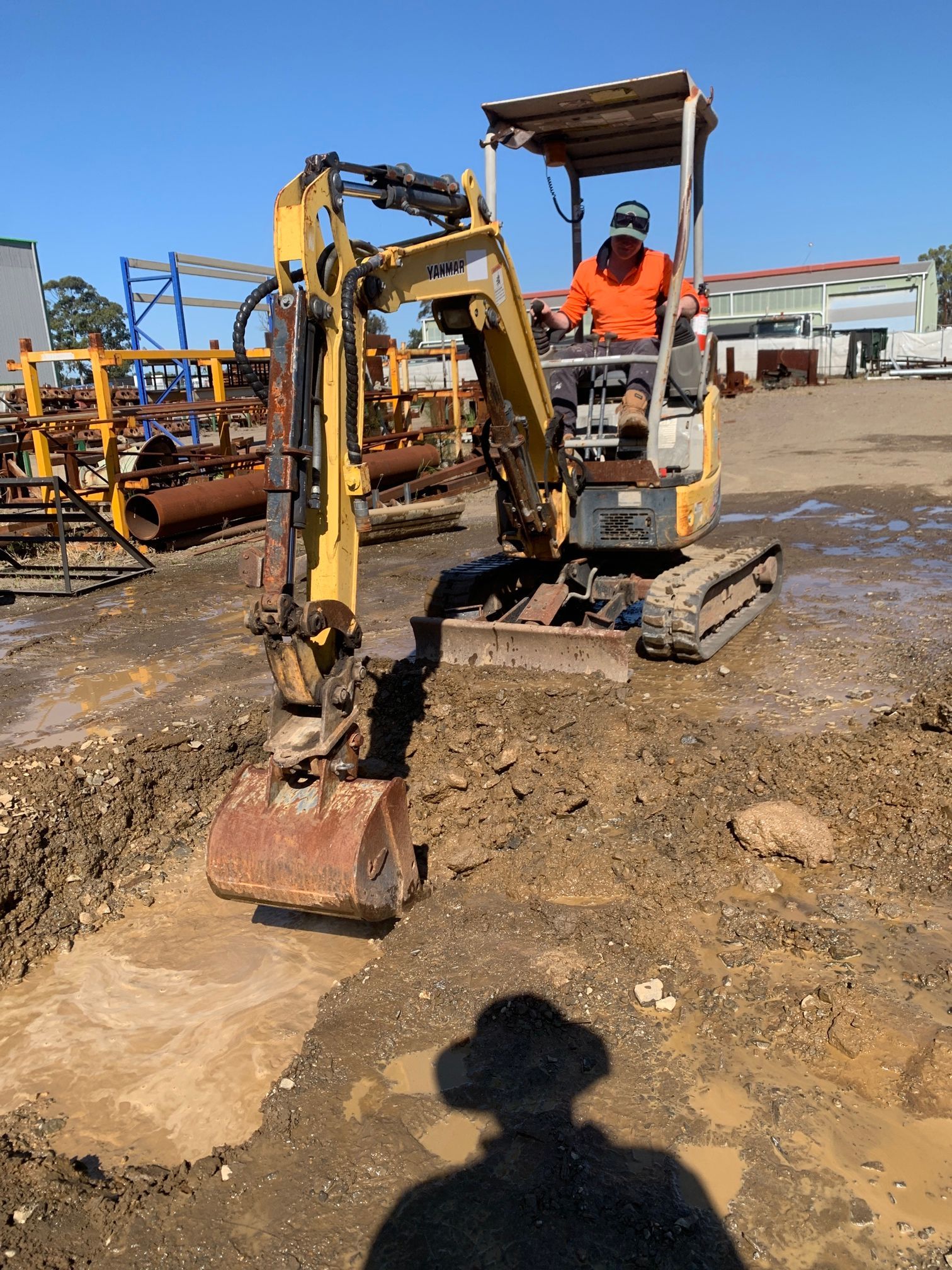 Worker in orange gear operating a small excavator at a construction site  — Huddo's Plumbing Service in Wallalong, NSW