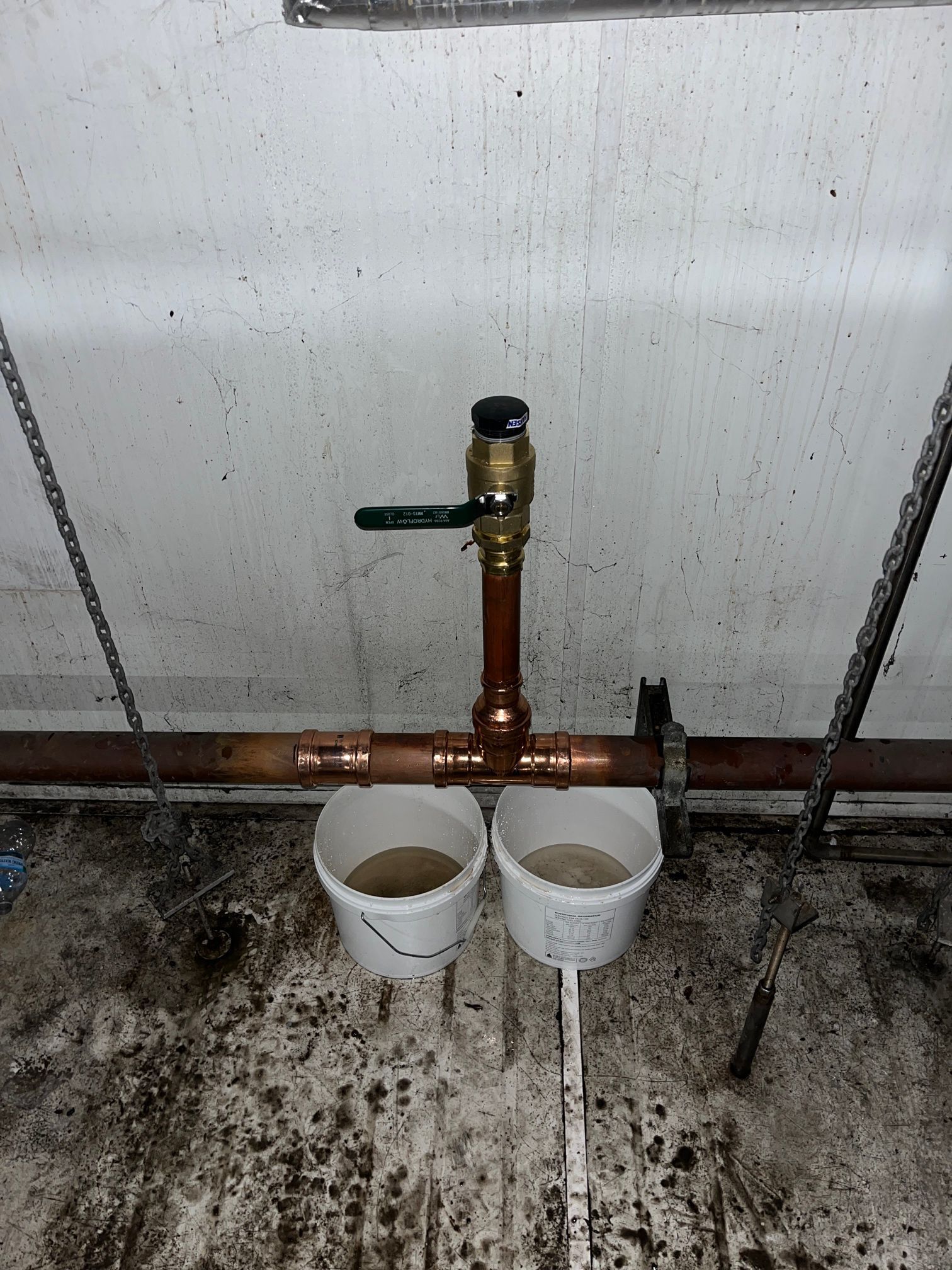 Copper pipe with a valve above two white buckets collecting water indoors  — Huddo's Plumbing Service in Wallalong, NSW