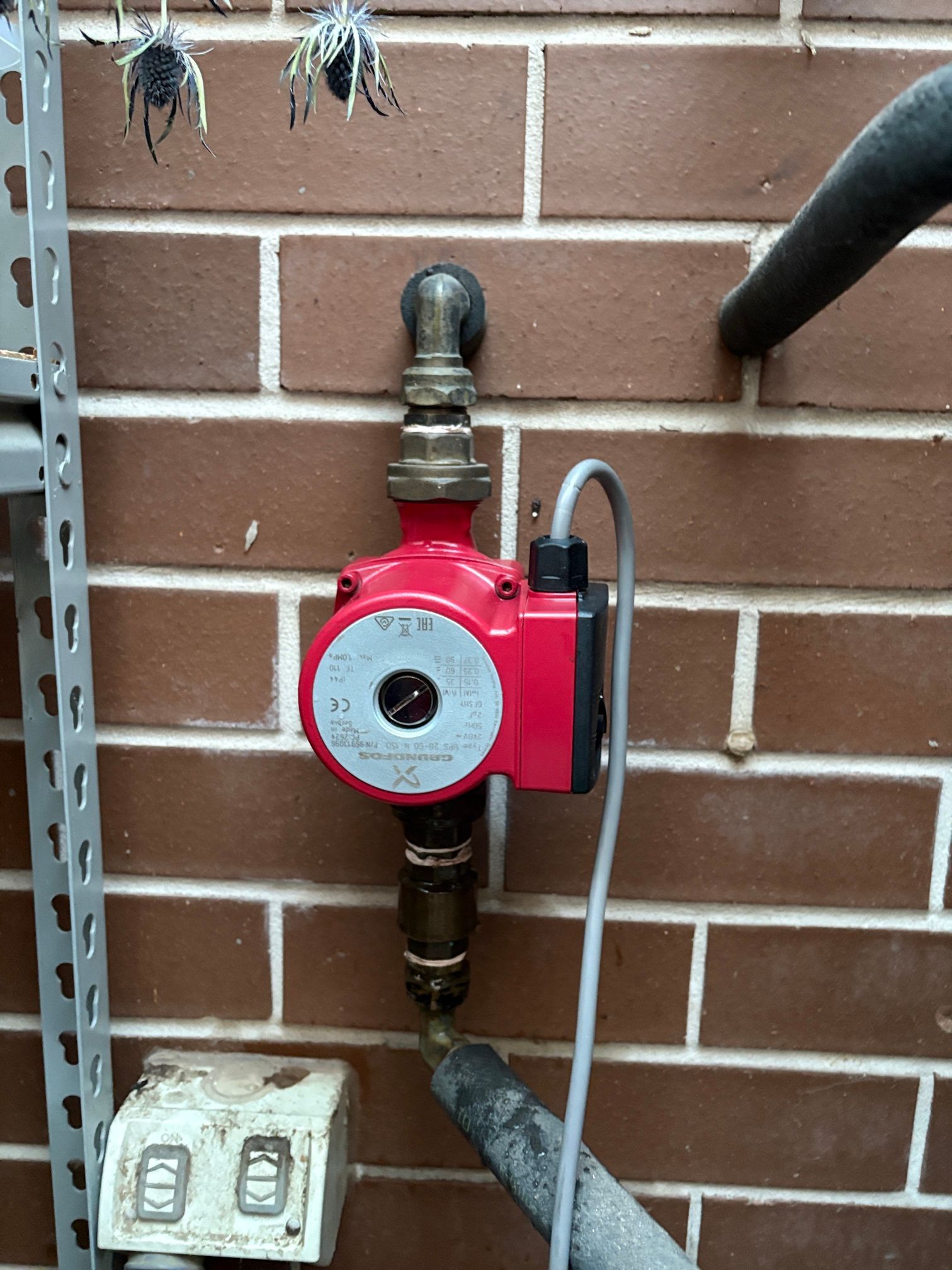 Red Water Pump Mounted on a Brick Wall With Pipes — Huddo's Plumbing Service in Wallalong, NSW
