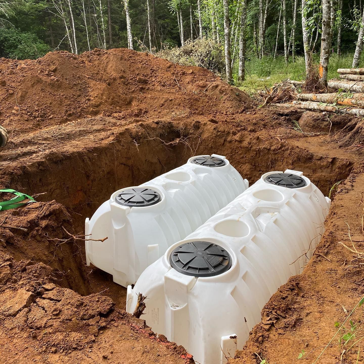Two white underground water tanks installed in a dirt excavation at a wooded site