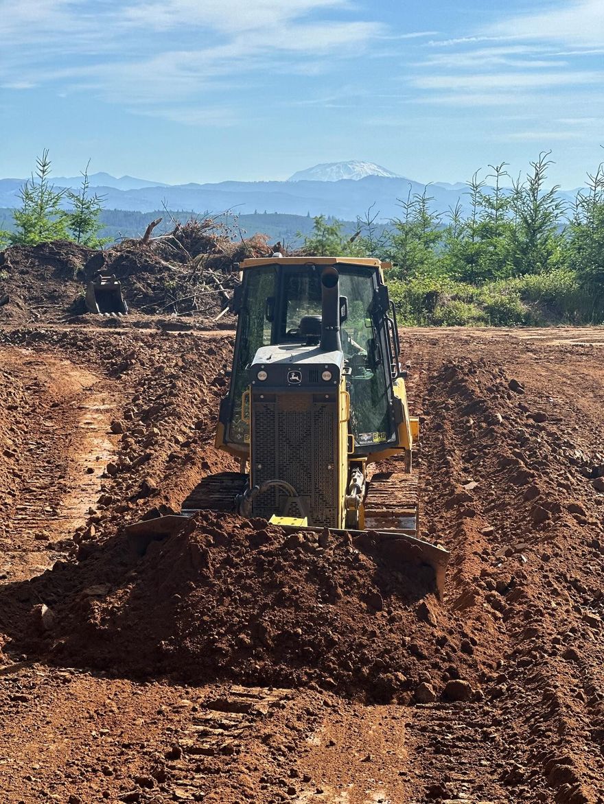 Yellow bulldozer pushing dirt on a muddy construction site with mountains in the background