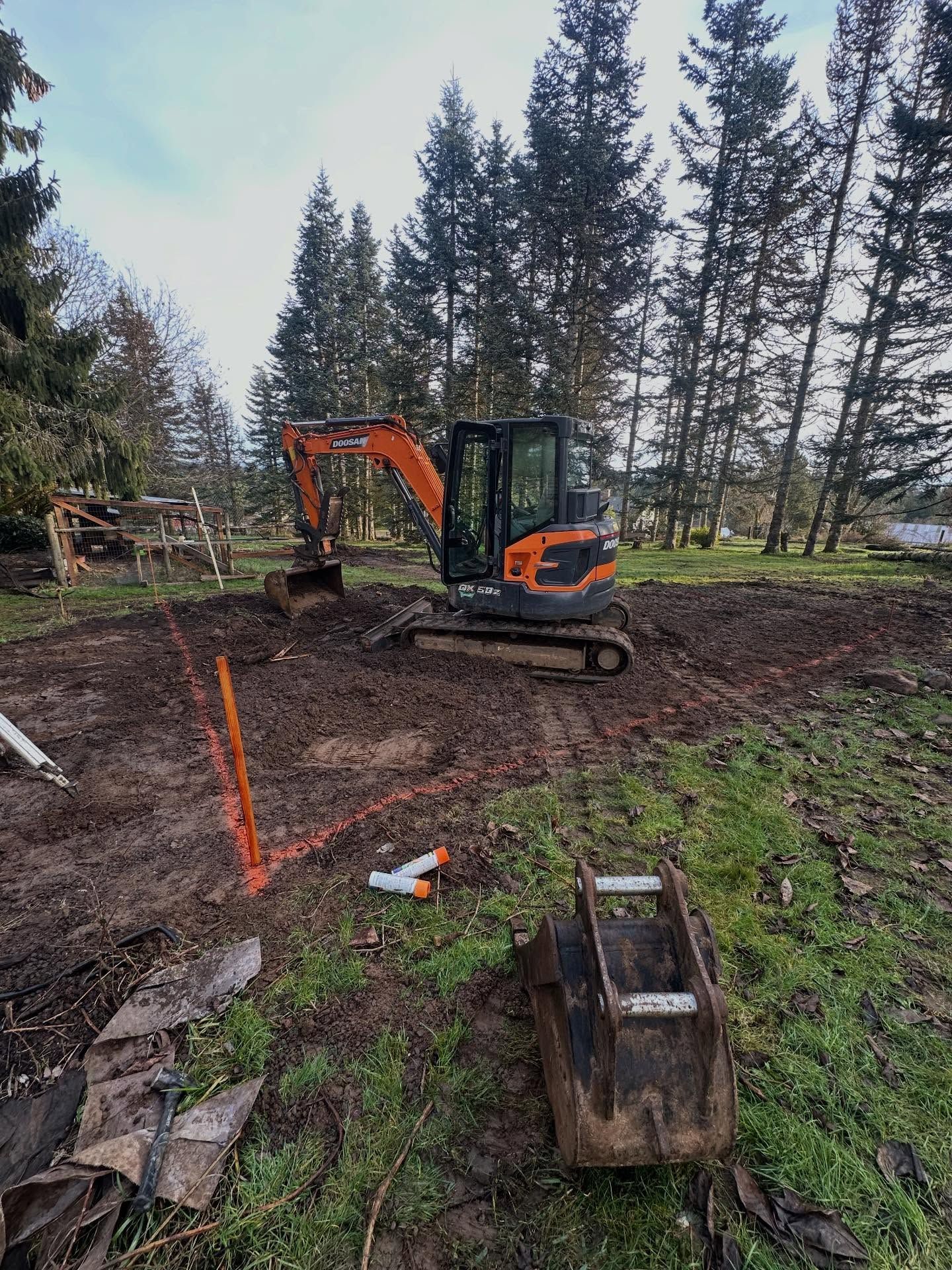 Orange excavator on a muddy construction site near trees and scattered tools