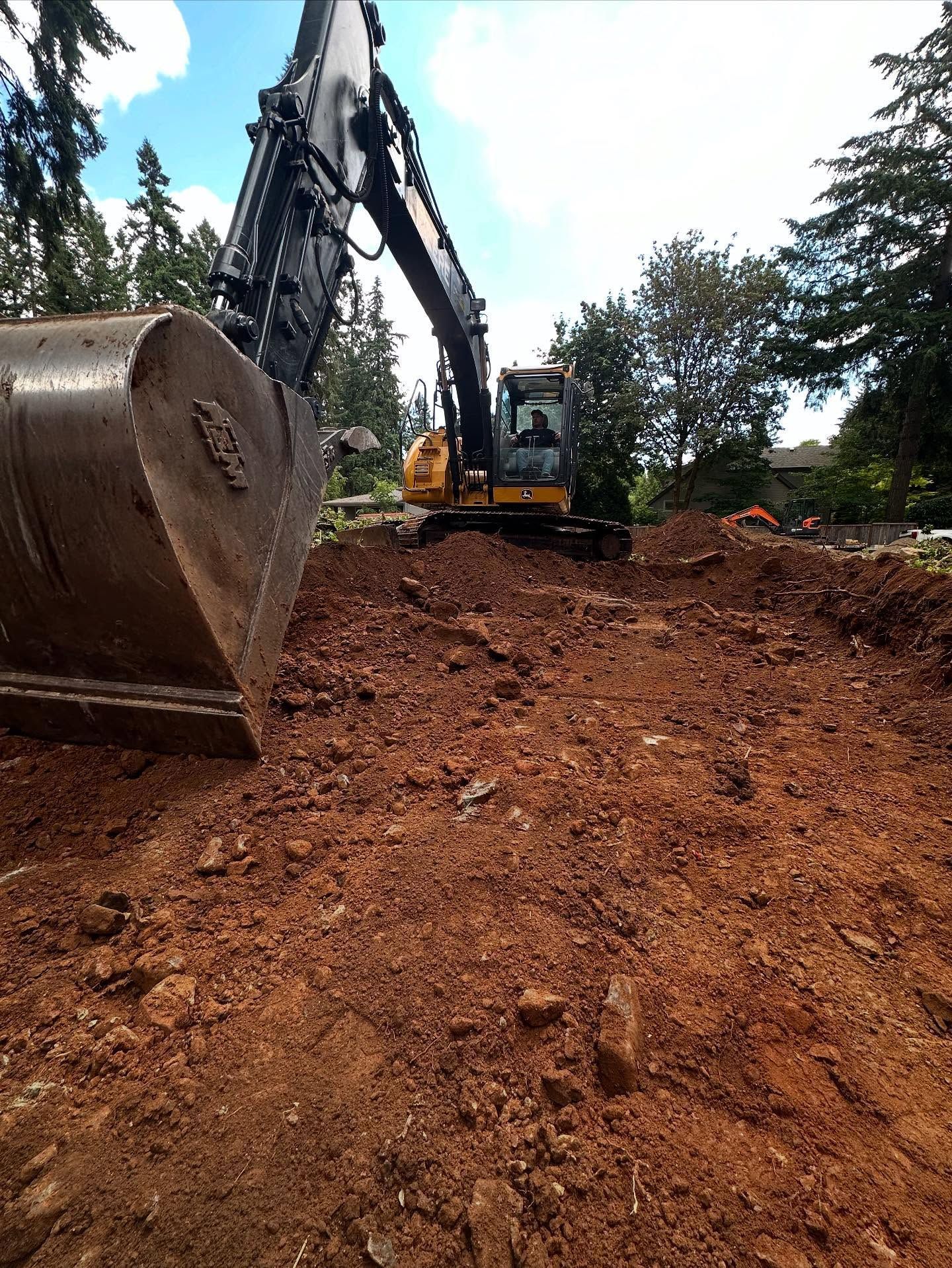 Excavator digging red soil on a construction site, with a large bucket in the foreground.