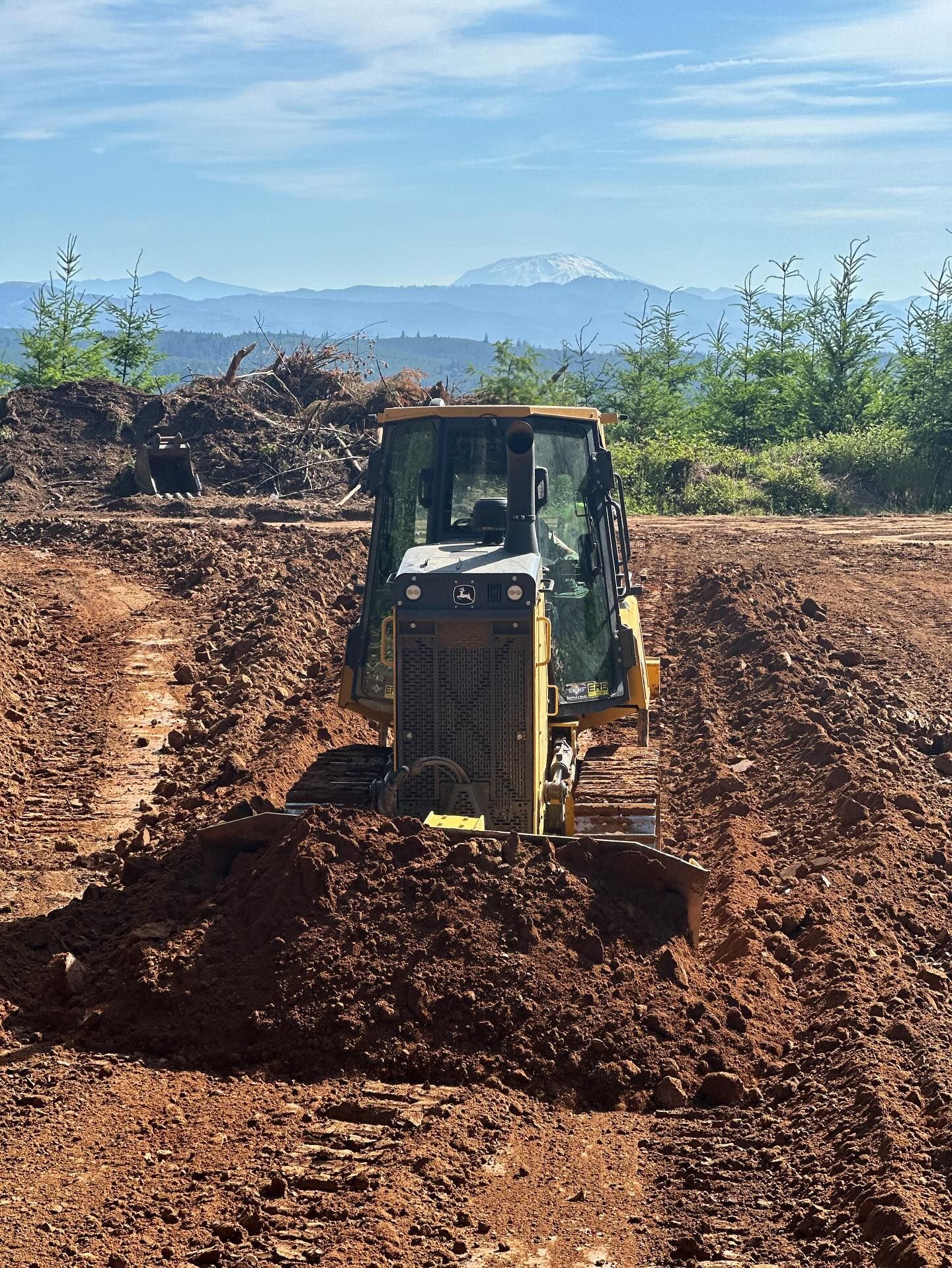 Bulldozer pushing dirt on a construction site with mountains in the background.
